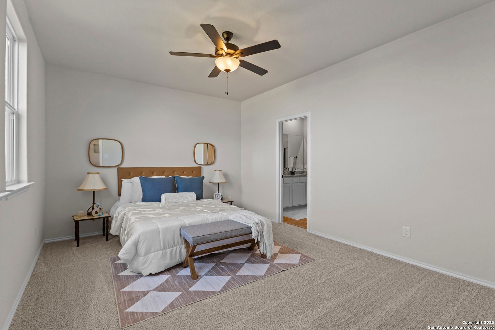 Bright bedroom with king bed, blue pillows, ceiling fan, mirrors, and en-suite bath in Davidson Homes The Douglas C, Seguin, Texas