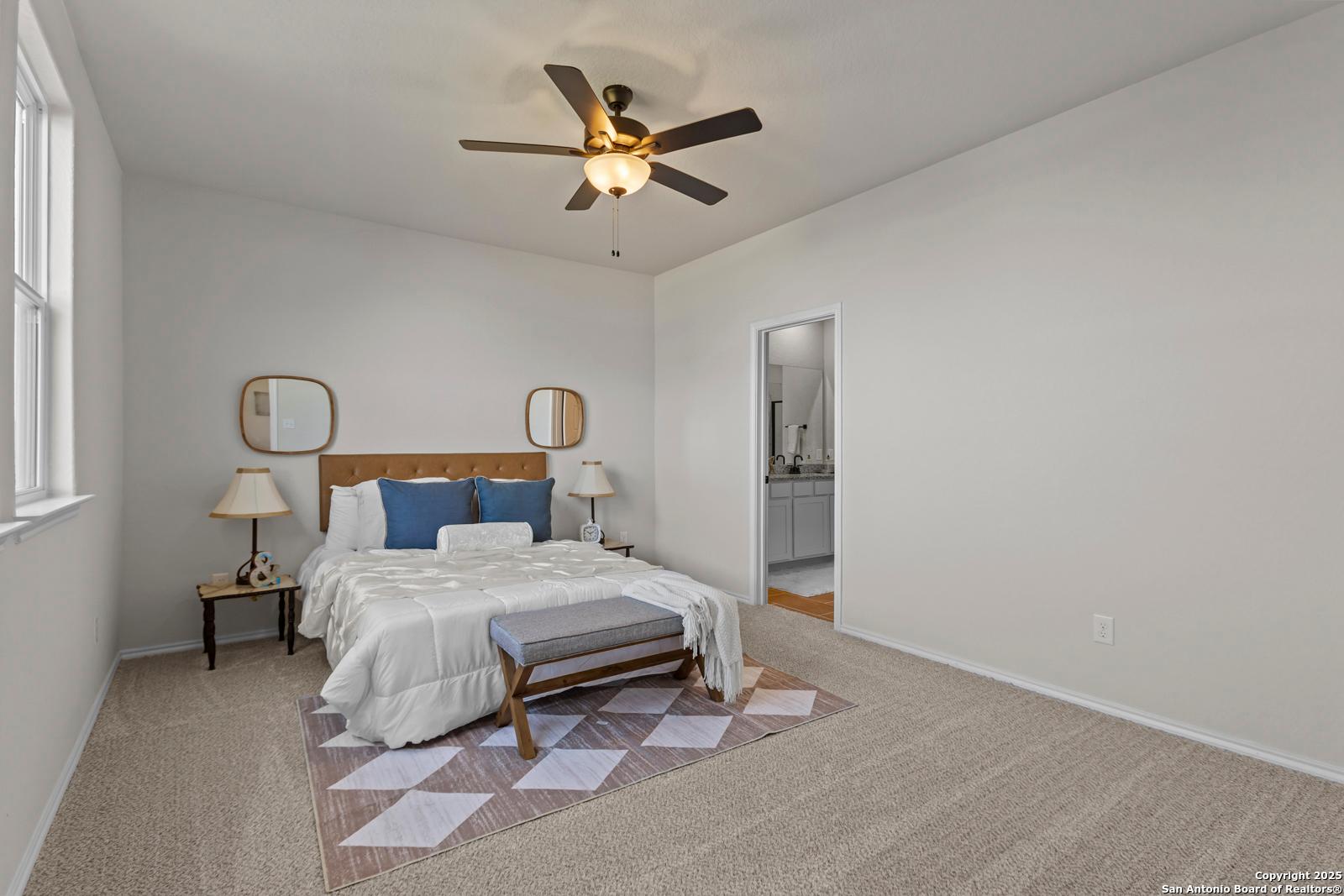 Bright bedroom with king bed, blue pillows, ceiling fan, mirrors, and en-suite bath in Davidson Homes The Douglas C, Seguin, Texas