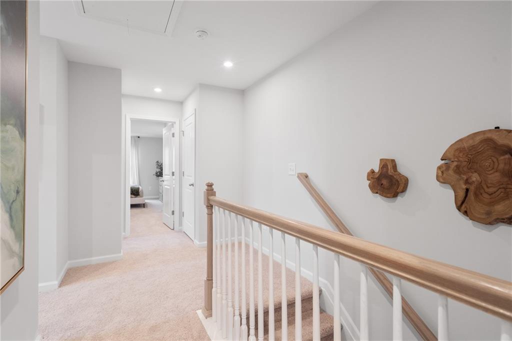 Upstairs hallway with oak staircase, light gray walls, carpeted floors, and wooden wall decor in The Wilmington B home, Emerson, Georgia