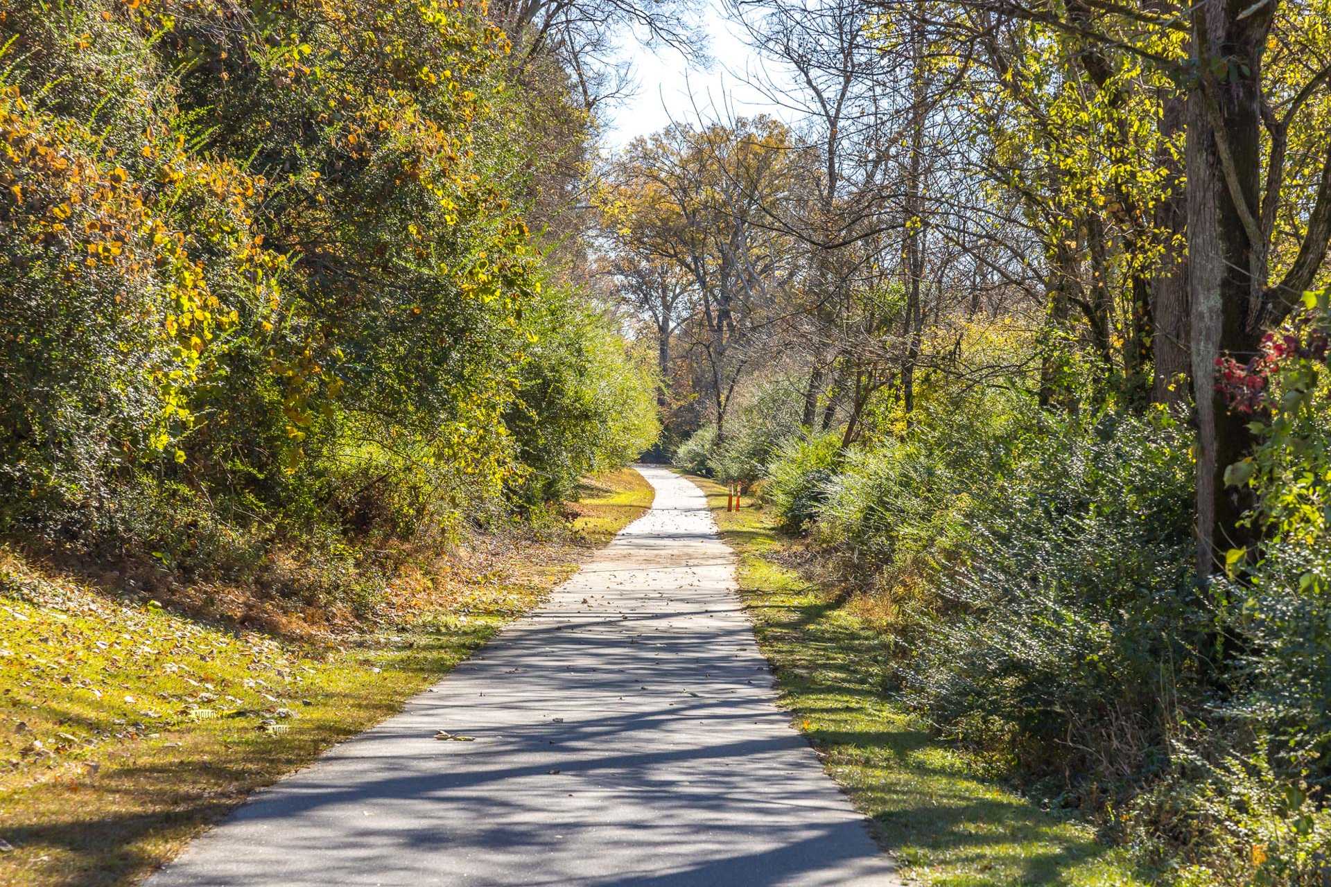 Sunlit paved walking trail through autumn foliage and woods at Sierra Heights in Clayton, NC
