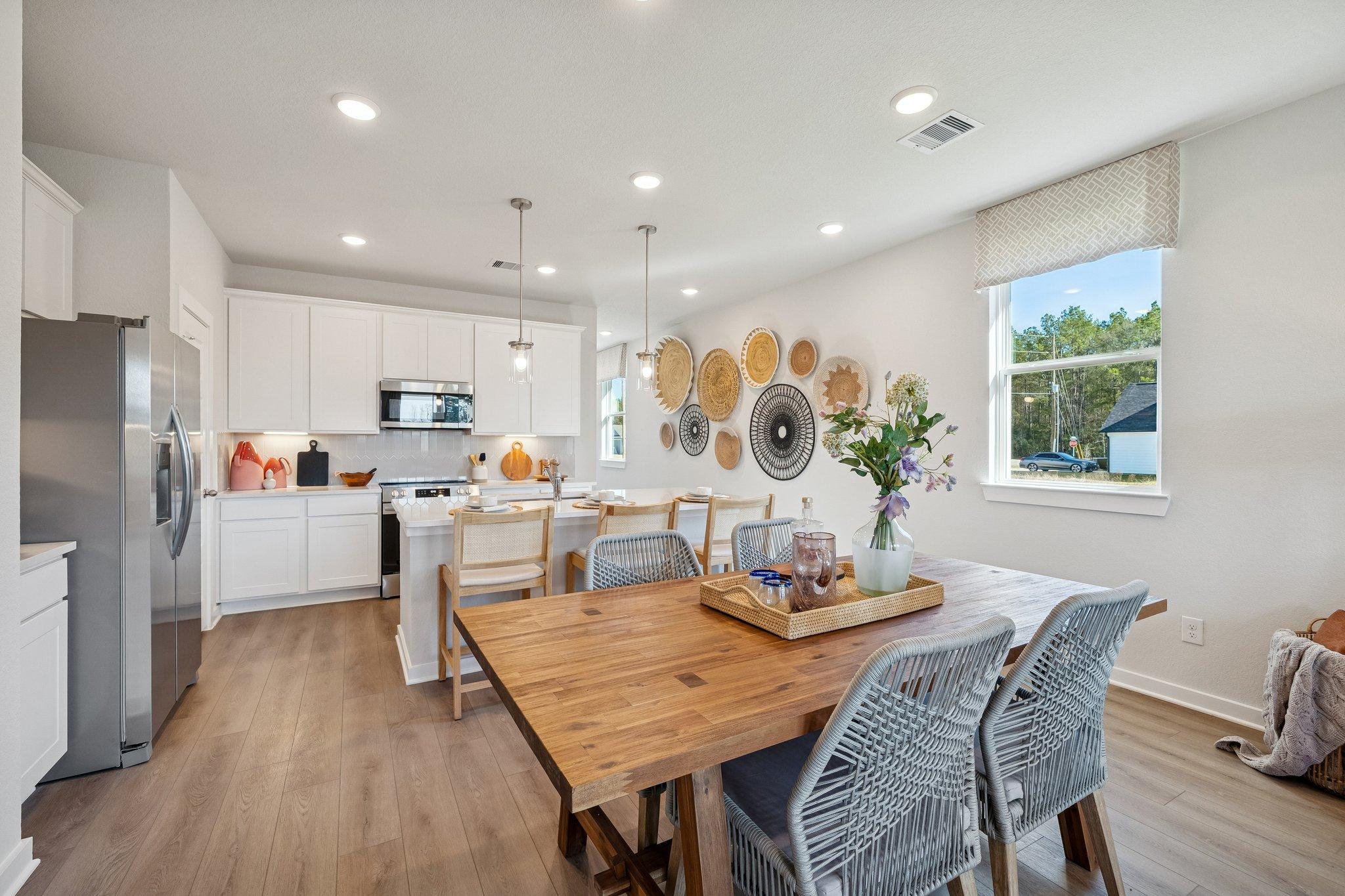 Open-concept kitchen dining area at Spring Branch Crossing in Conroe Texas with white cabinets wooden farmhouse table woven wall art
