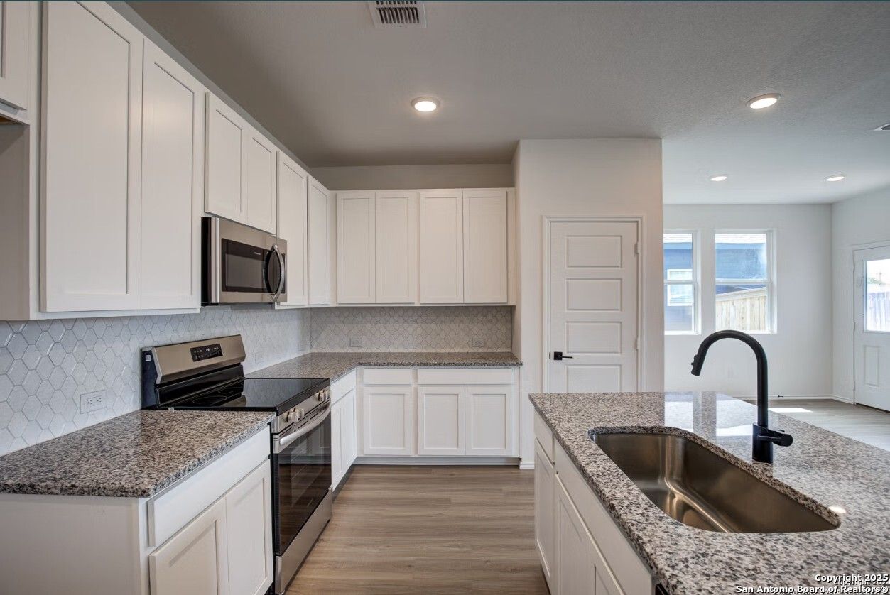 Modern white kitchen with granite countertops, stainless steel appliances, subway tile backsplash in Davidson Homes The Daphne H, Seguin, TX