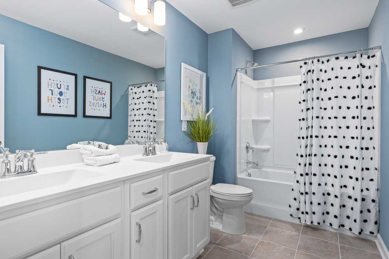 Spacious blue bathroom at Prince Place in Fuquay-Varina NC by Davidson Homes with double vanity, polka dot shower curtain, and modern fixtures