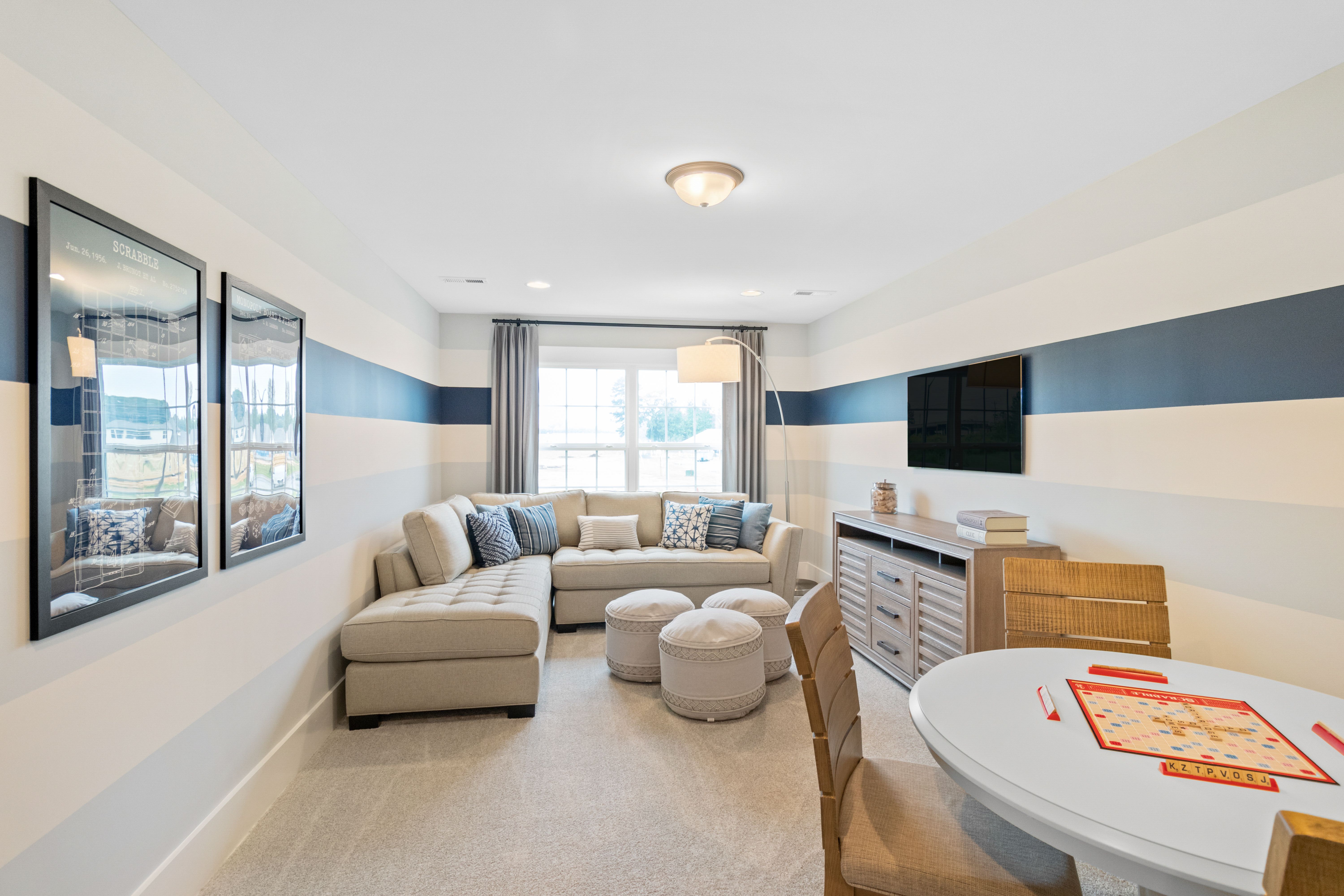Cozy family room in Noble Ridge Cullman AL with L-shaped beige sofa, striped walls, round game table, and large windows