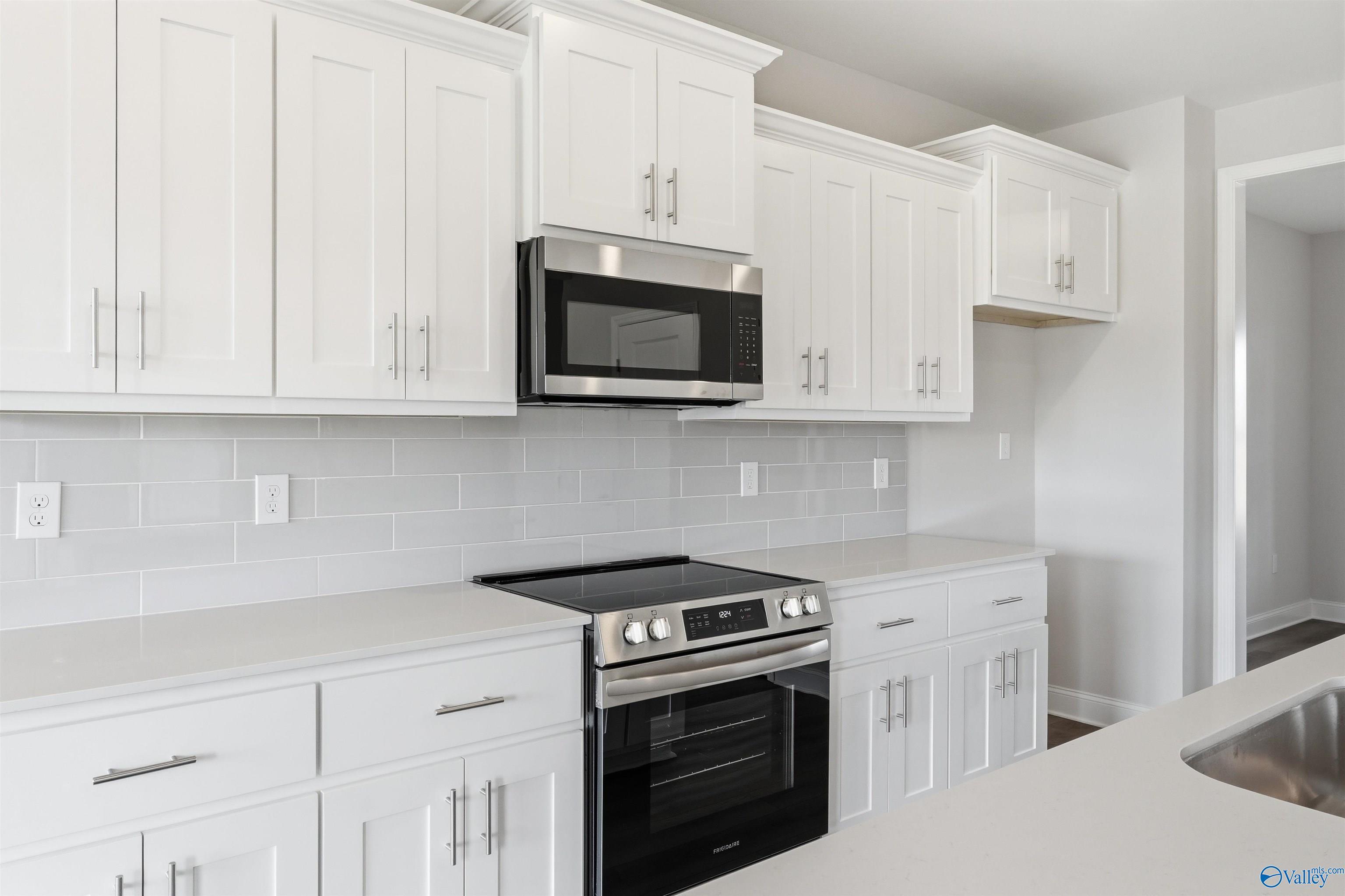 Modern kitchen with white shaker cabinets, quartz countertops, and stainless appliances in The Shelby D home, Madison, AL.