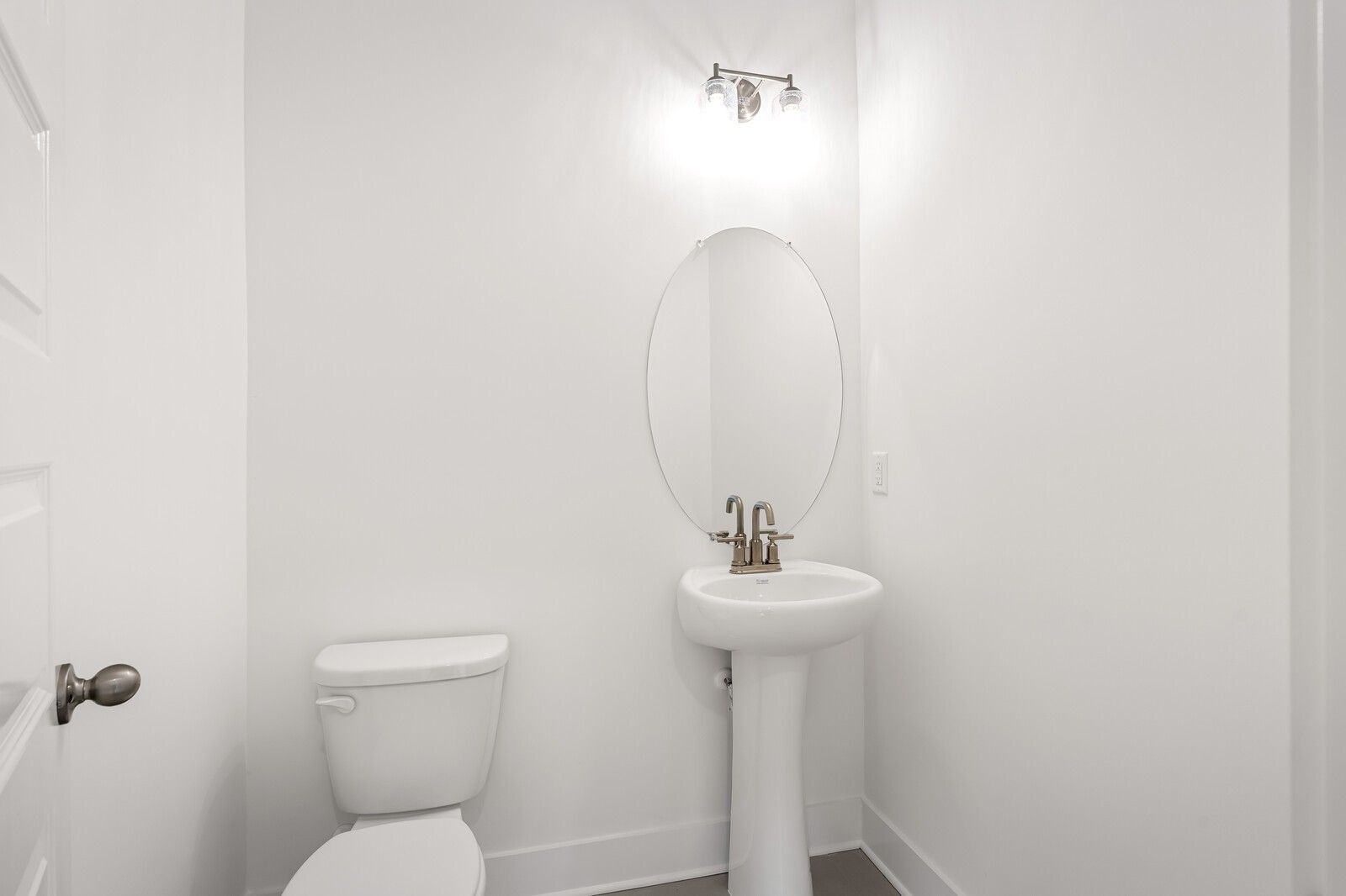 Bright white powder room with pedestal sink, round mirror, and sconce in Davidson Homes The Ash C, Mt. Juliet, TN