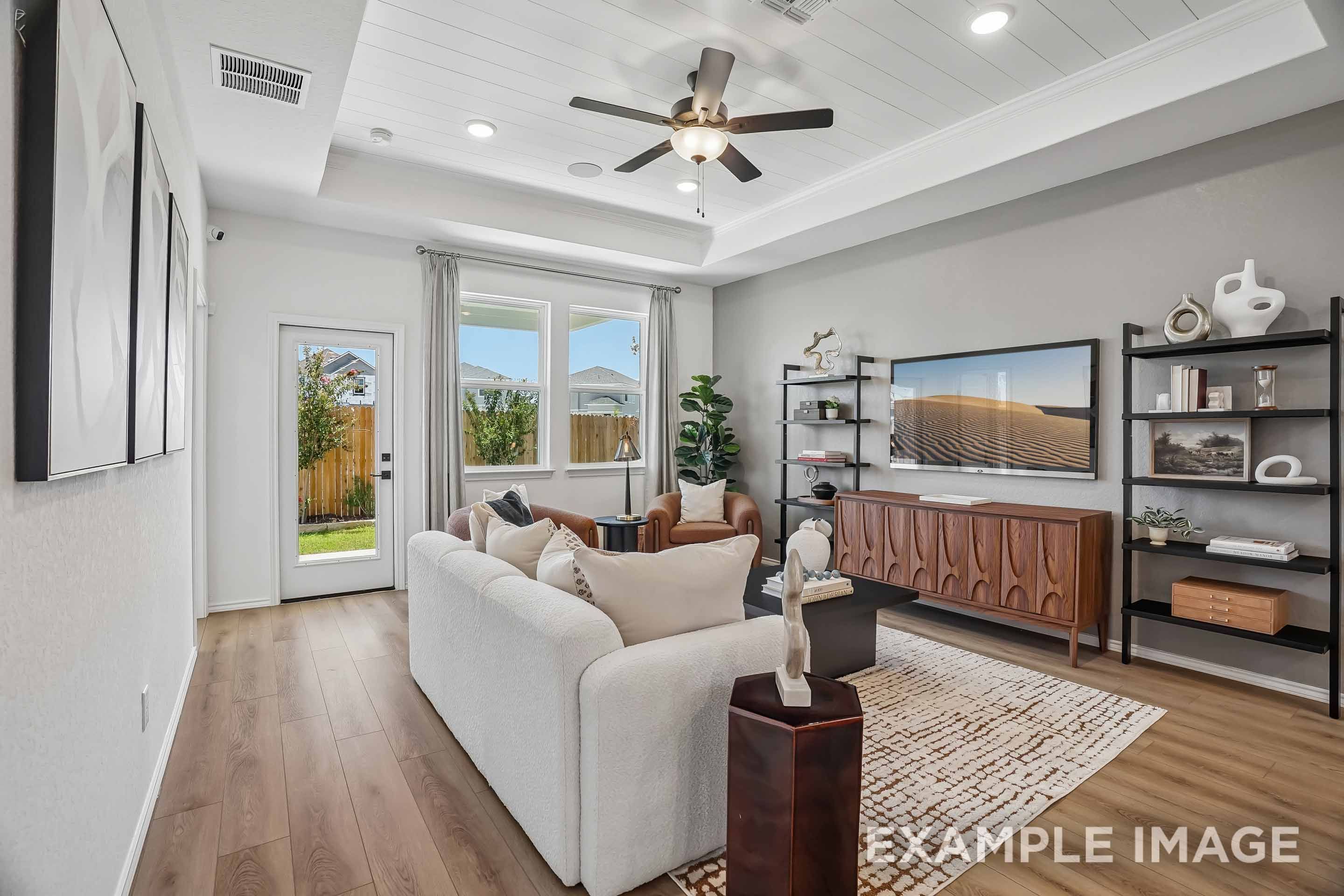Spacious living room in The Pinecrest B featuring a tray ceiling, modern decor, and wood flooring in San Antonio, Texas.