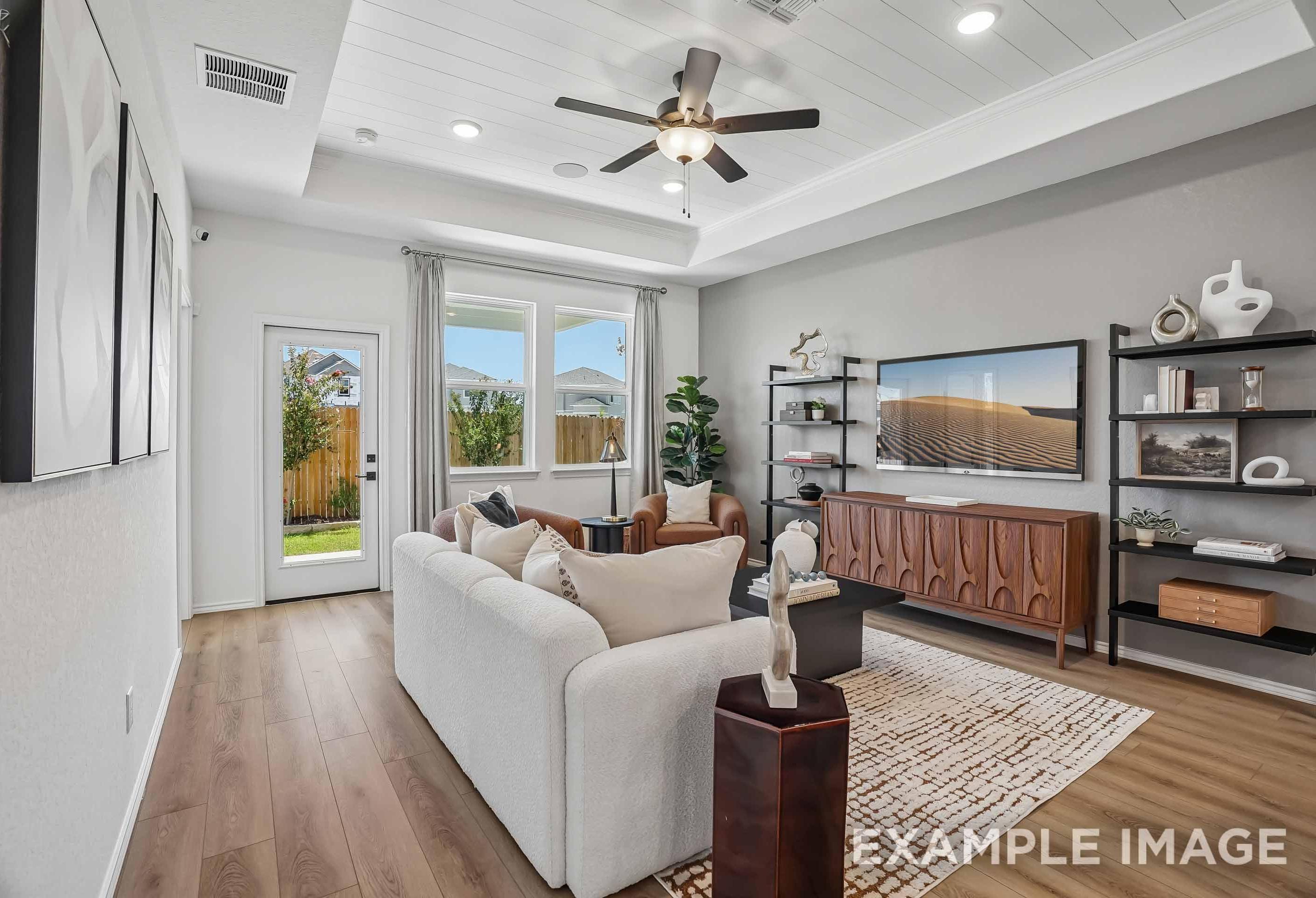 Spacious living room in The Pinecrest B featuring a tray ceiling, modern decor, and wood flooring in San Antonio, Texas.