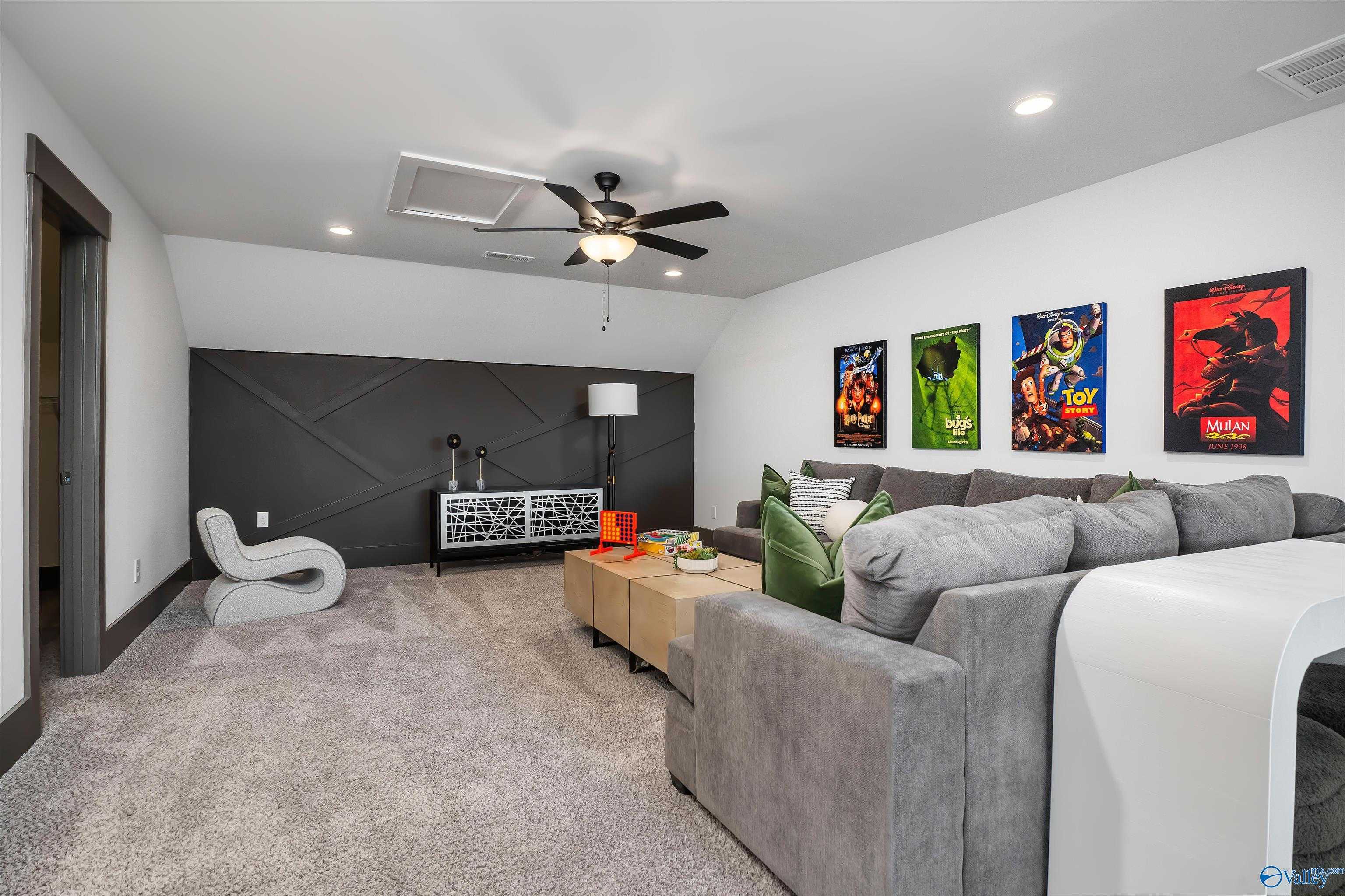 Cozy bonus room with gray sectional sofa, movie posters on black accent wall, and ceiling fan in Davidson Homes The Rockford B, Madison AL