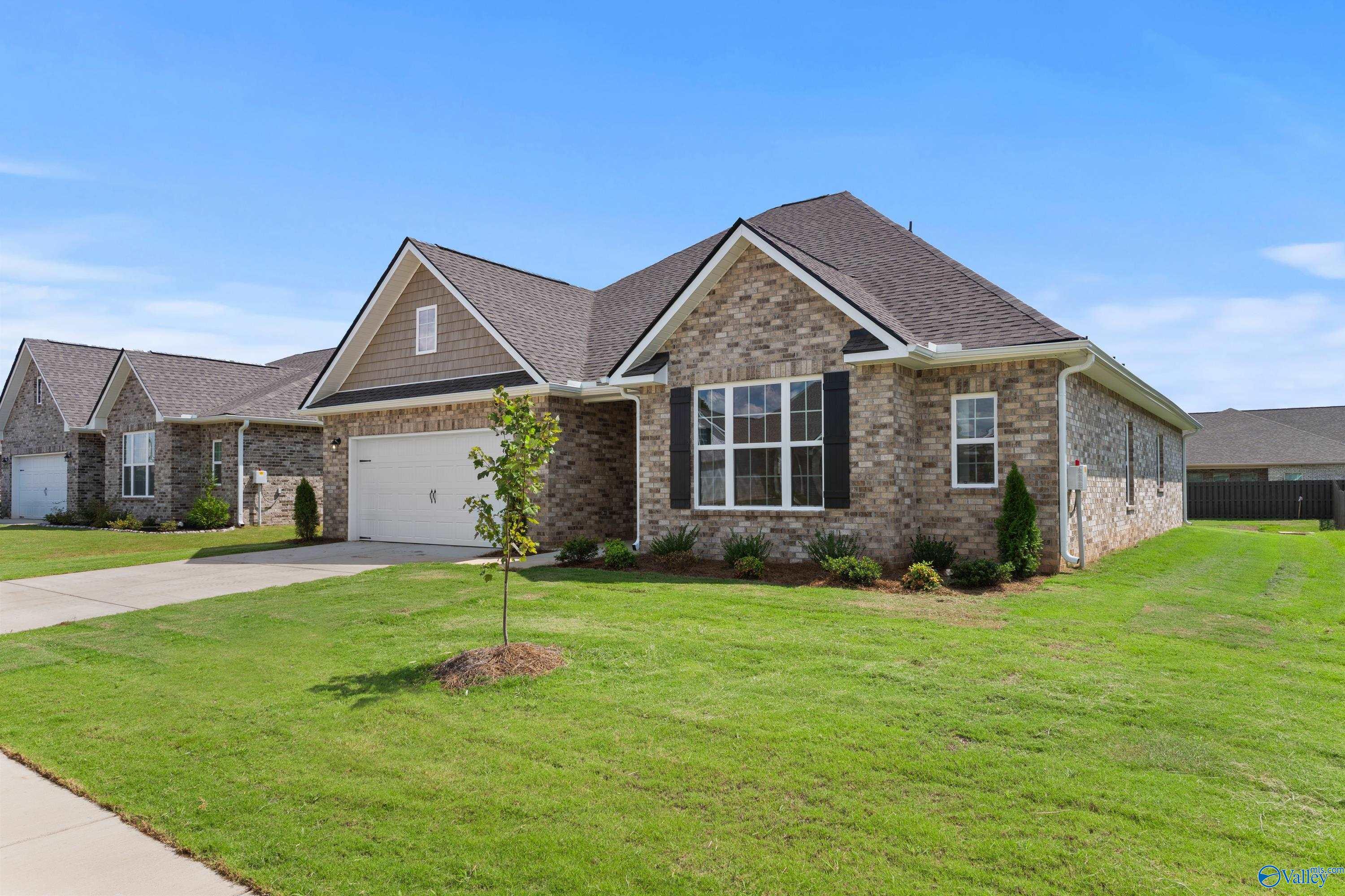Brick 1.5-story home with 2-car garage, green lawn, and blue sky in Kendall Downs, Toney, Alabama by Davidson Homes