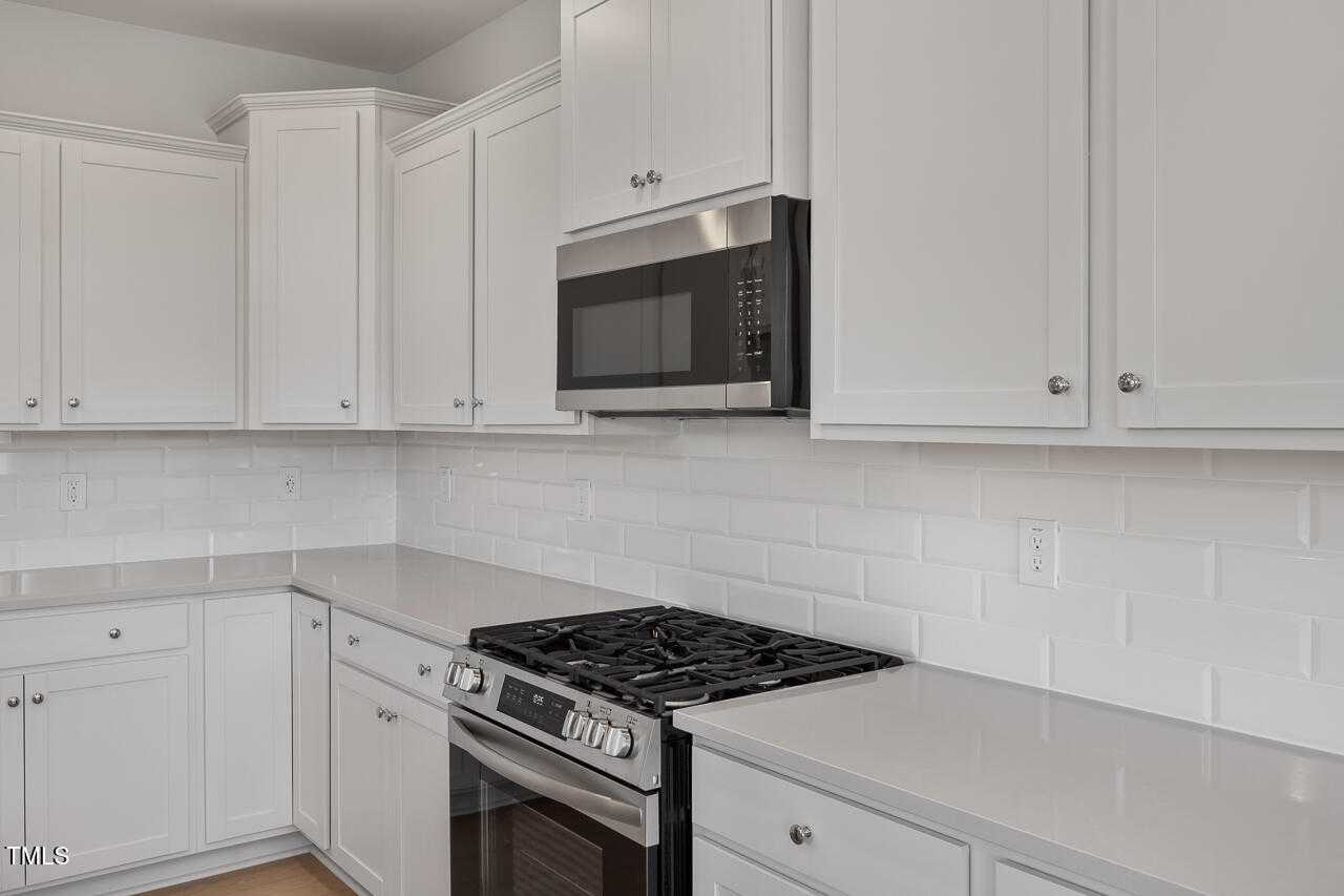 Modern white shaker kitchen with stainless gas range, oven, microwave, subway tile backsplash in Davidson Homes The Graham, Fuquay-Varina, NC