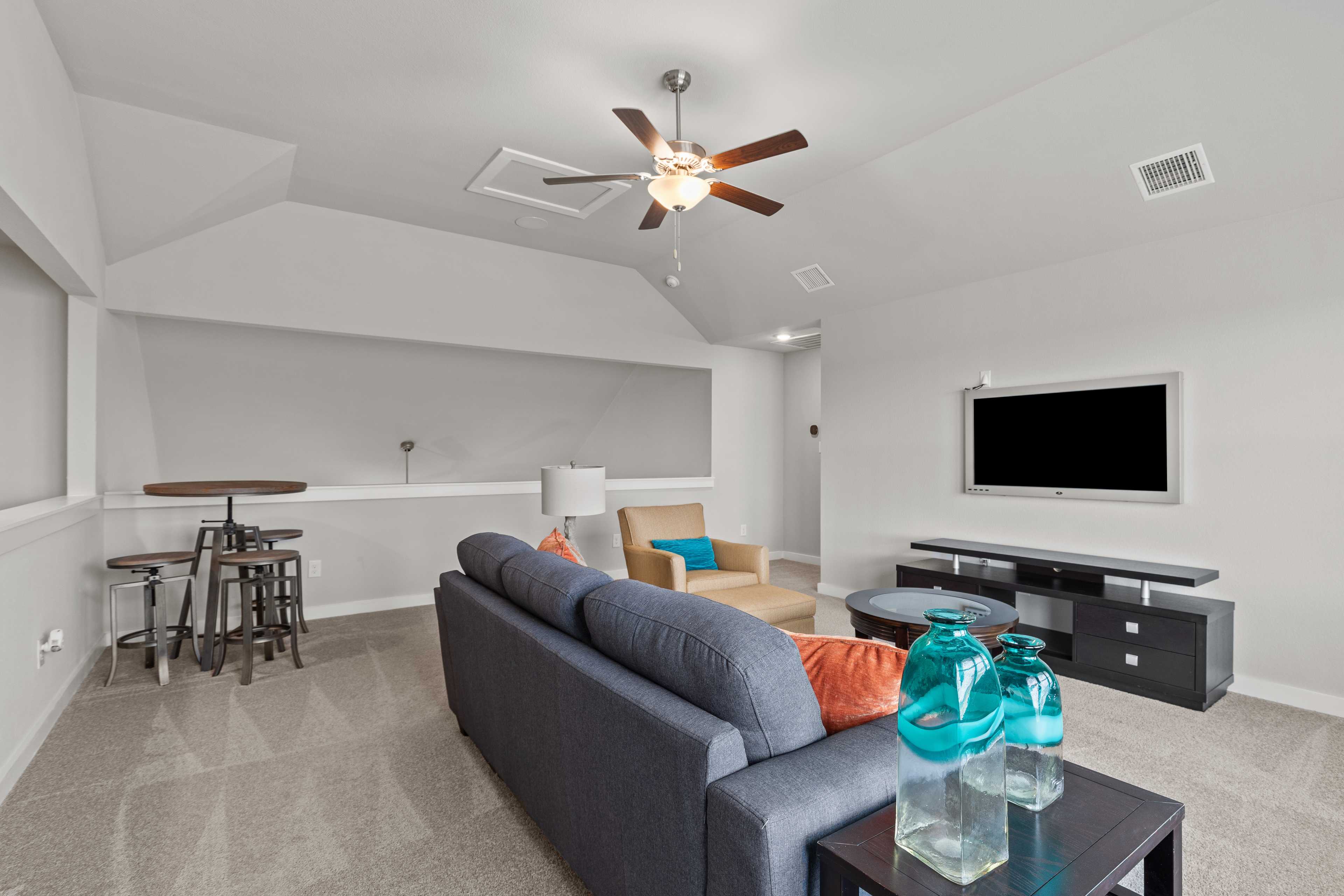 Spacious media room at Hannah Heights in Seguin Texas with navy sofa, flat-screen TV, bar stools, and ceiling fan by Davidson Homes