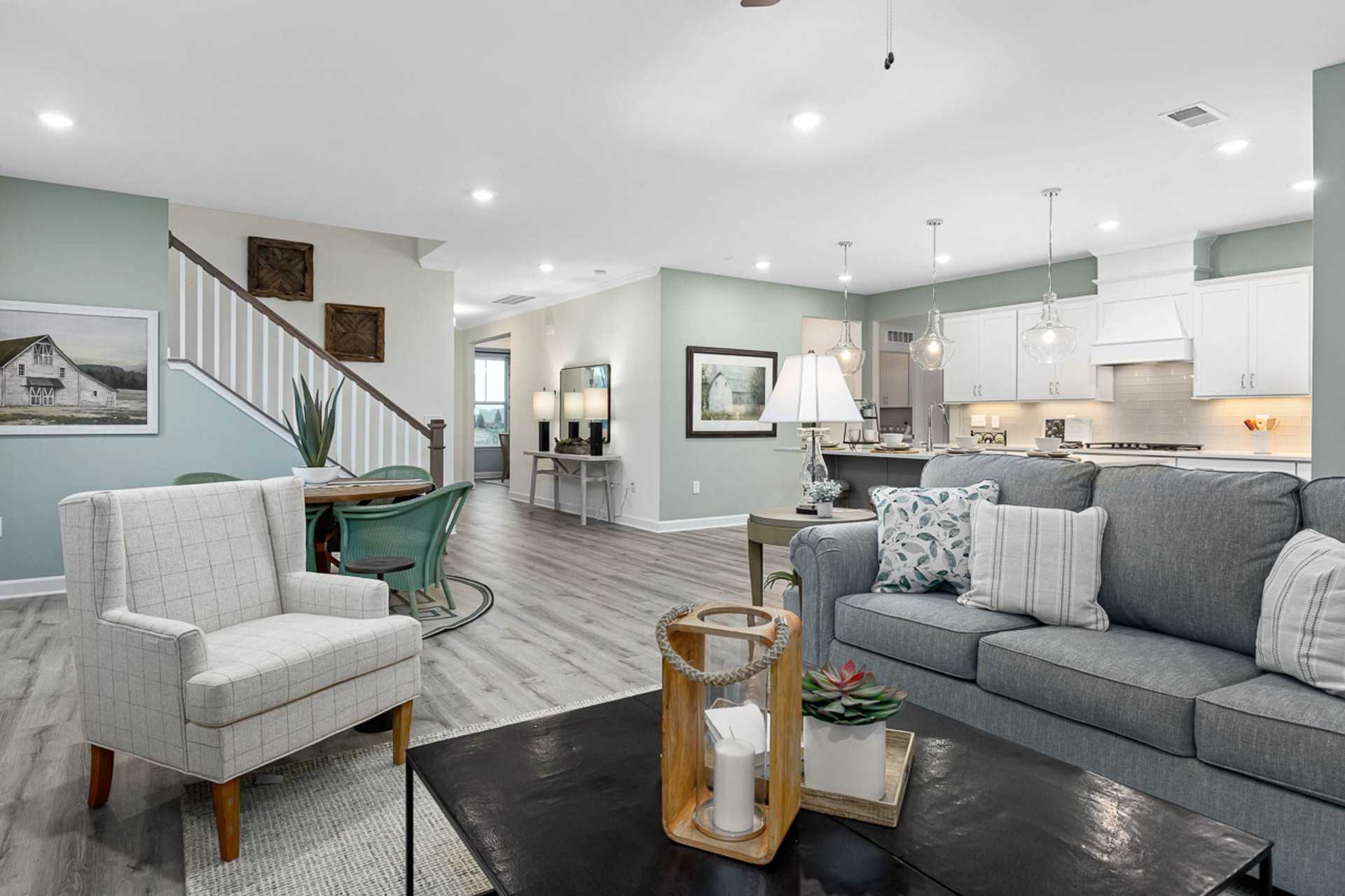 Open-concept living room in Bentwinds Fuquay-Varina NC by Davidson Homes featuring gray sectional sofa, light wood floors, and modern kitchen island