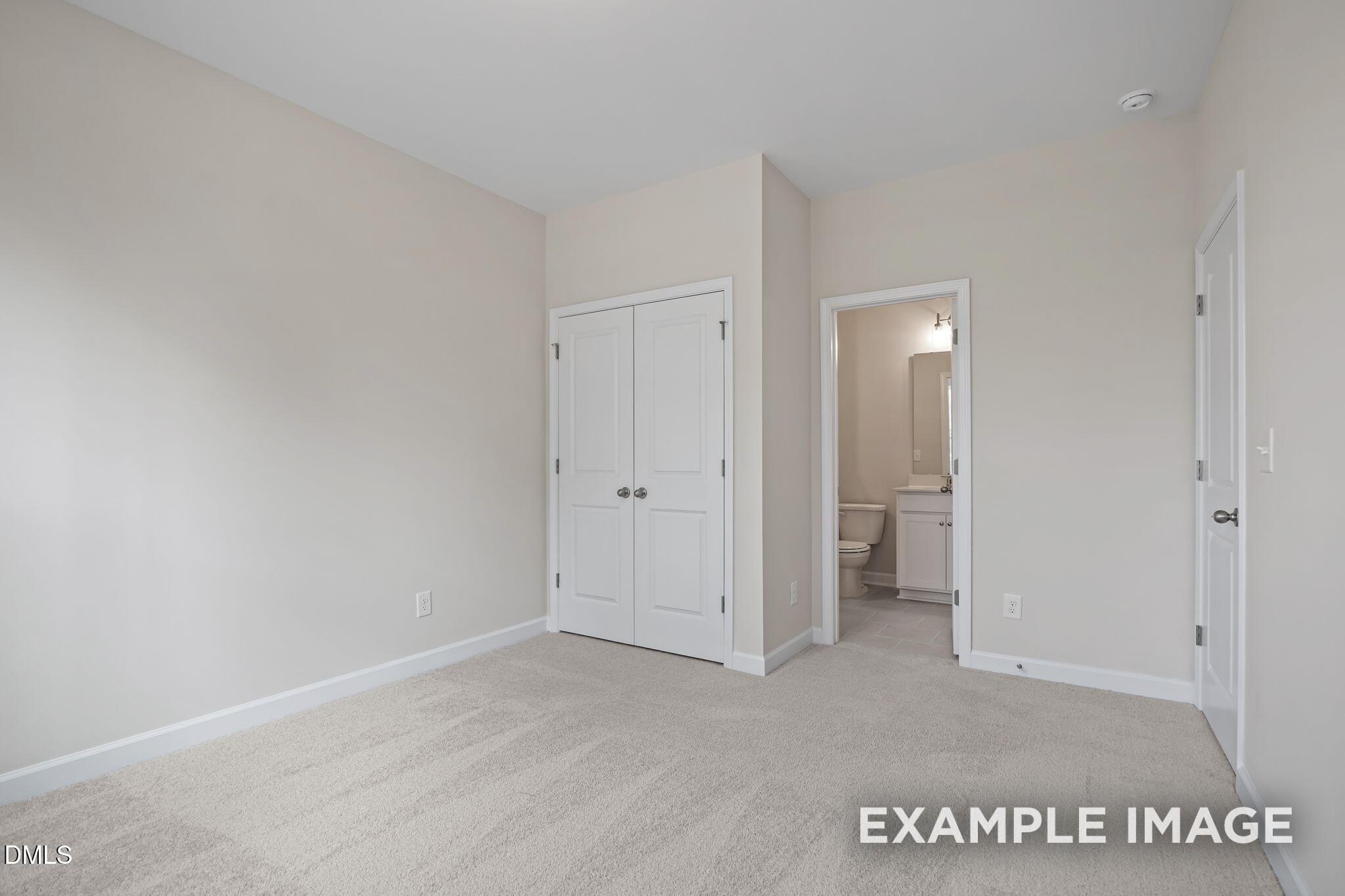 Spacious bedroom with beige walls, plush carpet flooring, double closet doors, and adjacent bathroom in Davidson Homes The Avery, Knightdale, NC