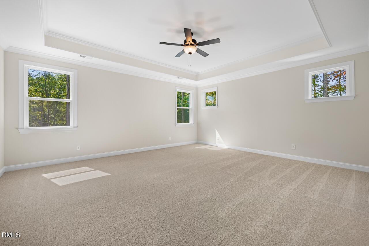 Bright spacious bedroom with tray ceiling, ceiling fan, carpet, and multiple windows in Davidson Homes The Crawford D, Wake Forest, NC