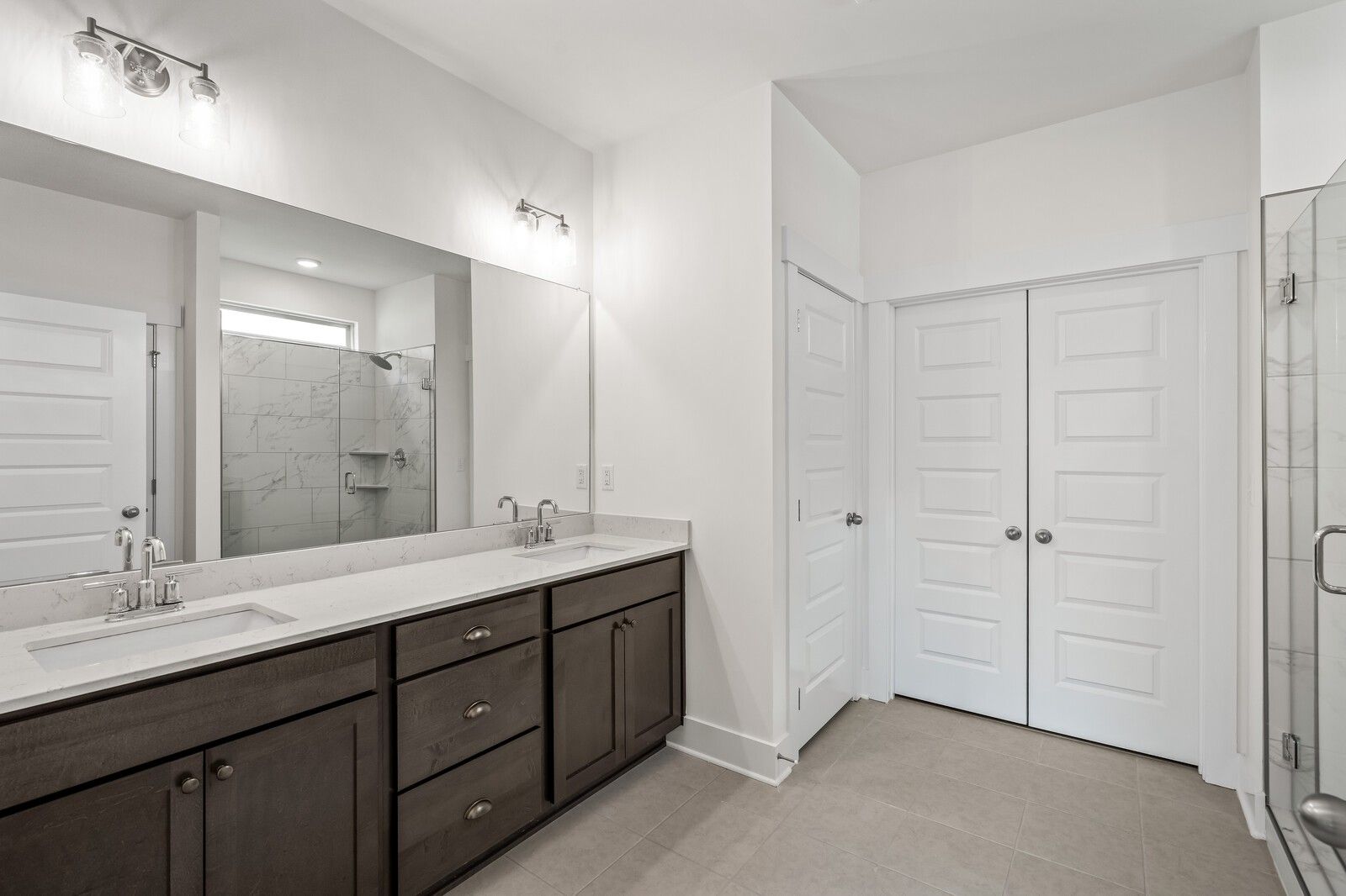 Modern primary bathroom with double vanity, walk-in shower, and storage in The Ridgeport C home at Woods Crossing, Gallatin.