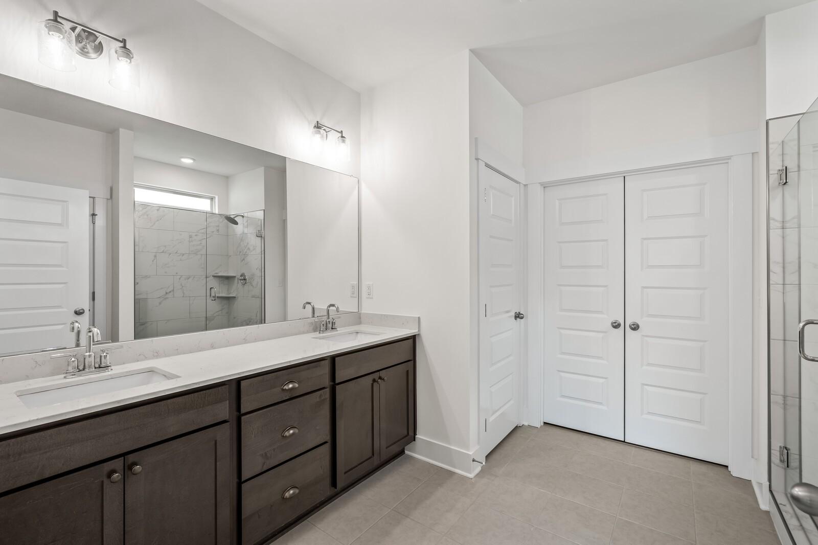 Modern primary bathroom with double vanity, walk-in shower, and storage in The Ridgeport C home at Woods Crossing, Gallatin.