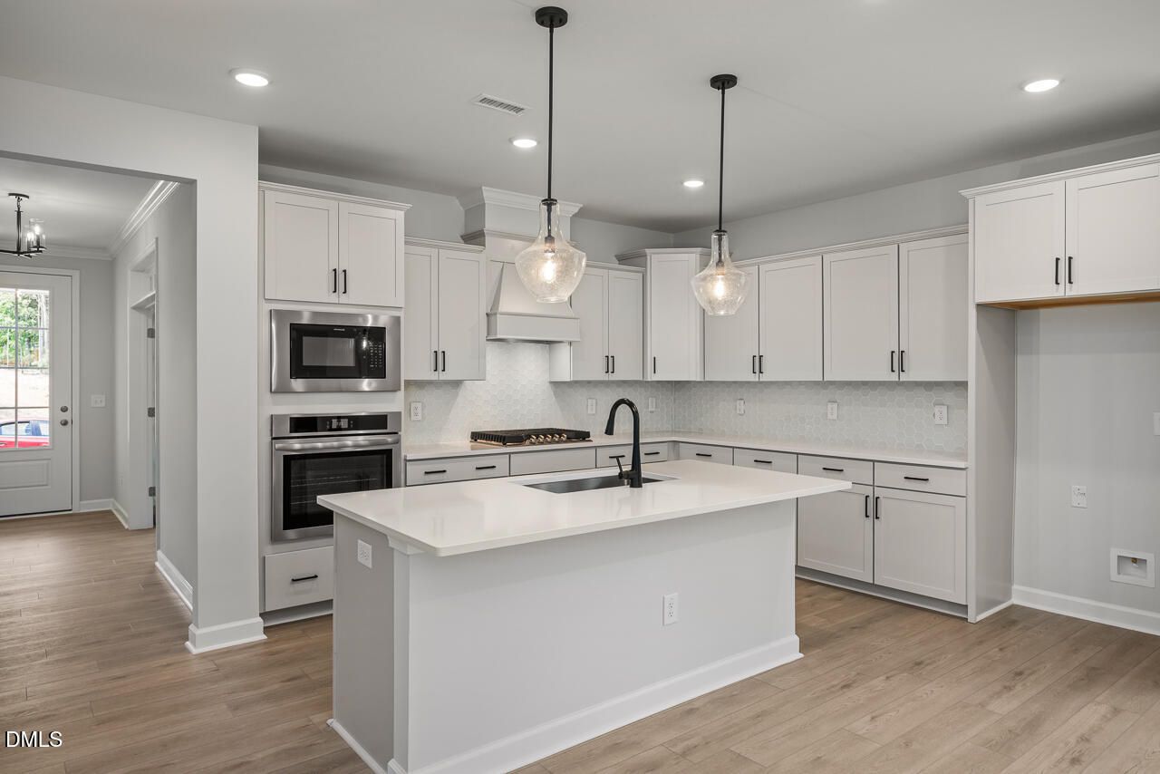 Modern white kitchen with island, quartz countertops, and stainless appliances in The Birch II E at Sage on North Main.