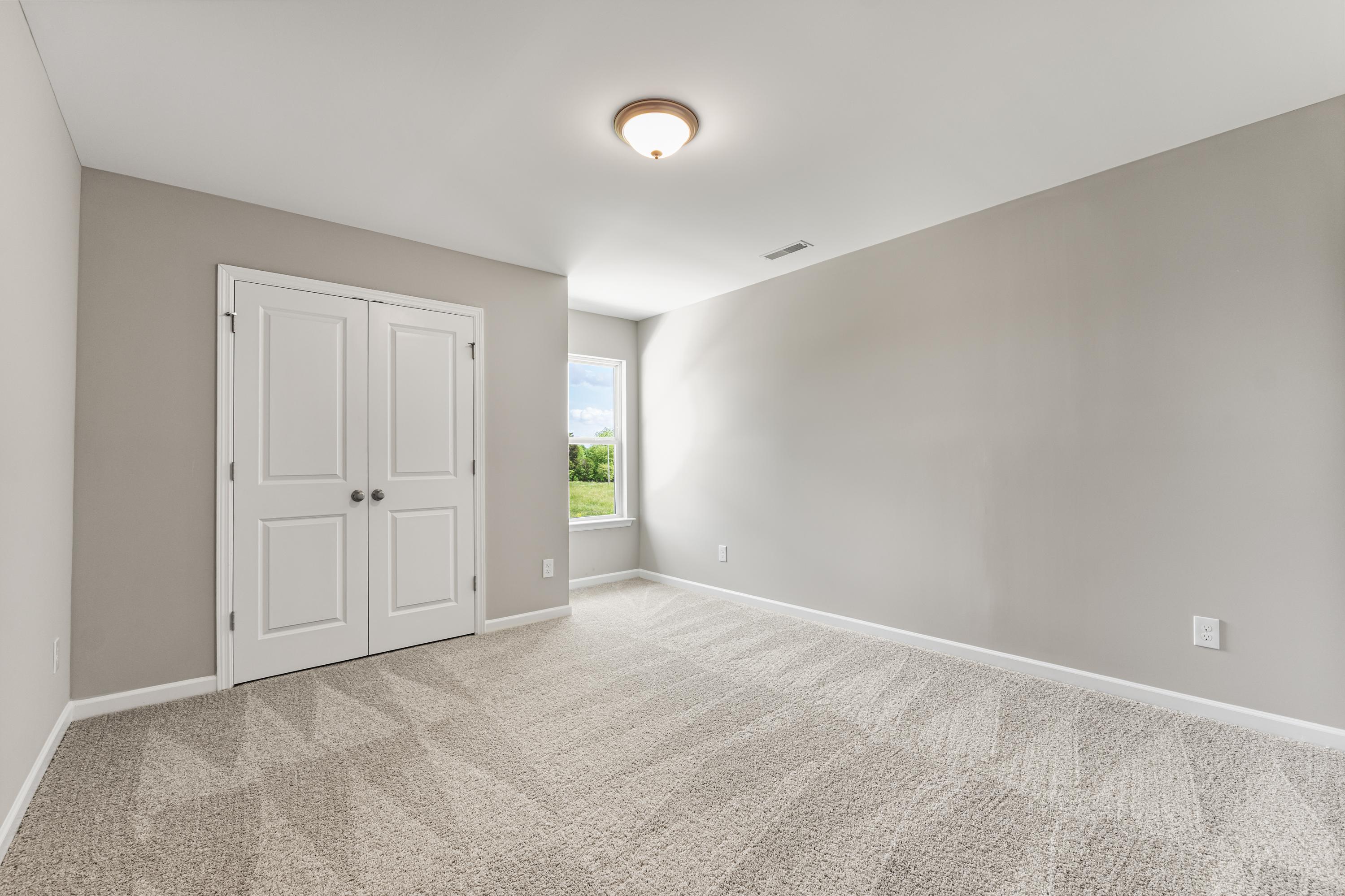 Spacious secondary bedroom in The Haven by Evermore Homes with light gray walls, white double closet doors, large window, and plush carpet