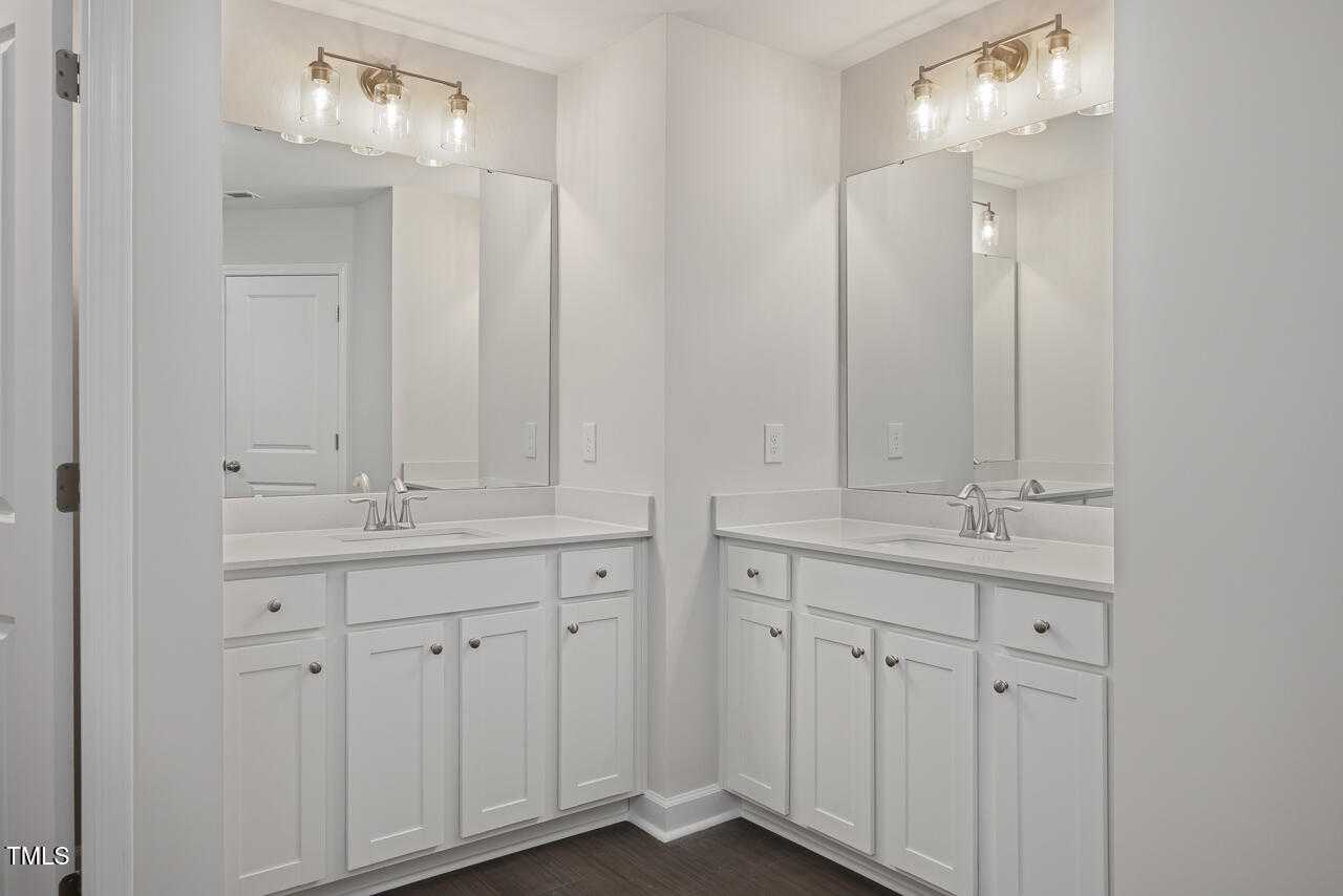 Elegant master bathroom double vanity with white shaker cabinets, gold sconces, and mirrors in Davidson Homes The Graham, Fuquay-Varina, NC