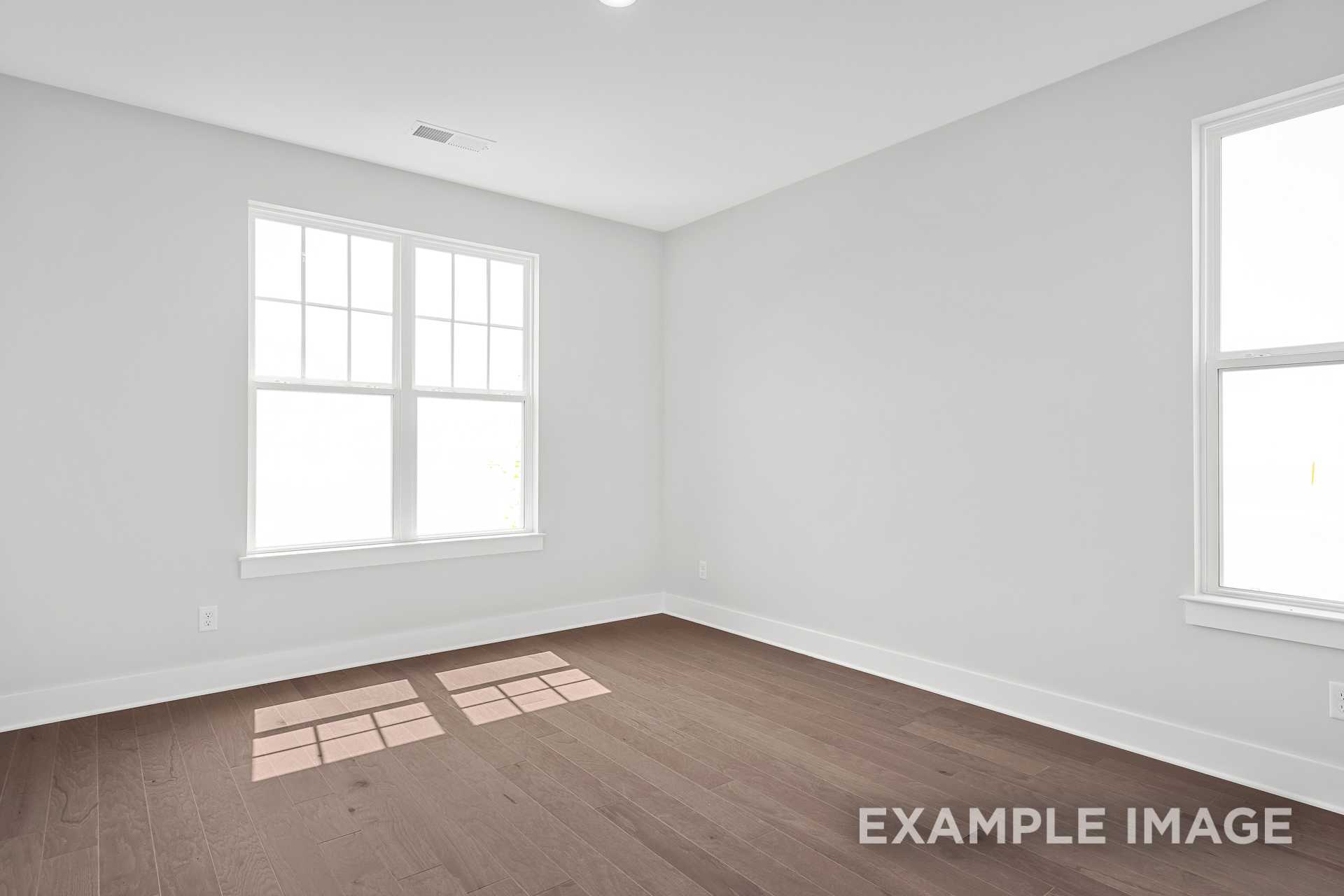 Spacious bedroom in The Hathaway featuring hardwood floors, large windows, and light gray walls