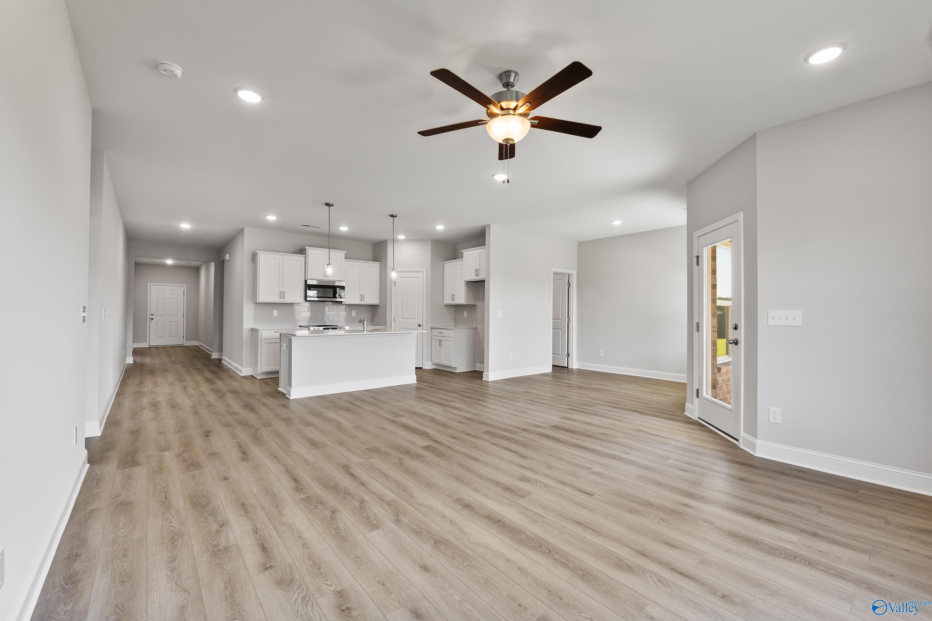 Open-concept kitchen-living space with white cabinets, island, ceiling fans, and luxury vinyl plank flooring in Davidson Homes The Daphne, Hazel Green, AL