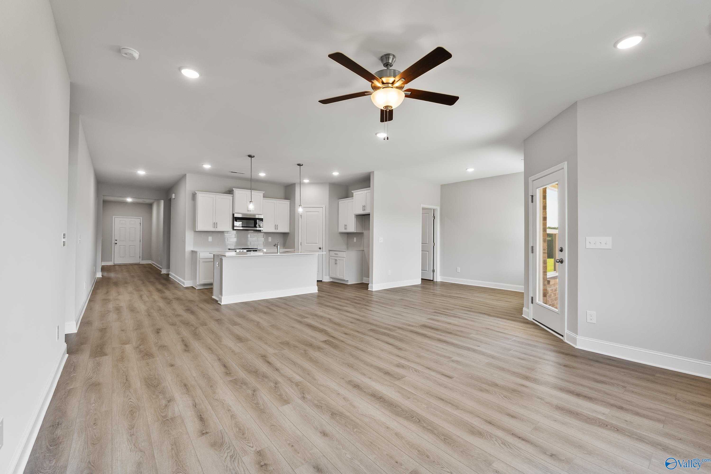 Open-concept kitchen-living space with white cabinets, island, ceiling fans, and luxury vinyl plank flooring in Davidson Homes The Daphne, Hazel Green, AL