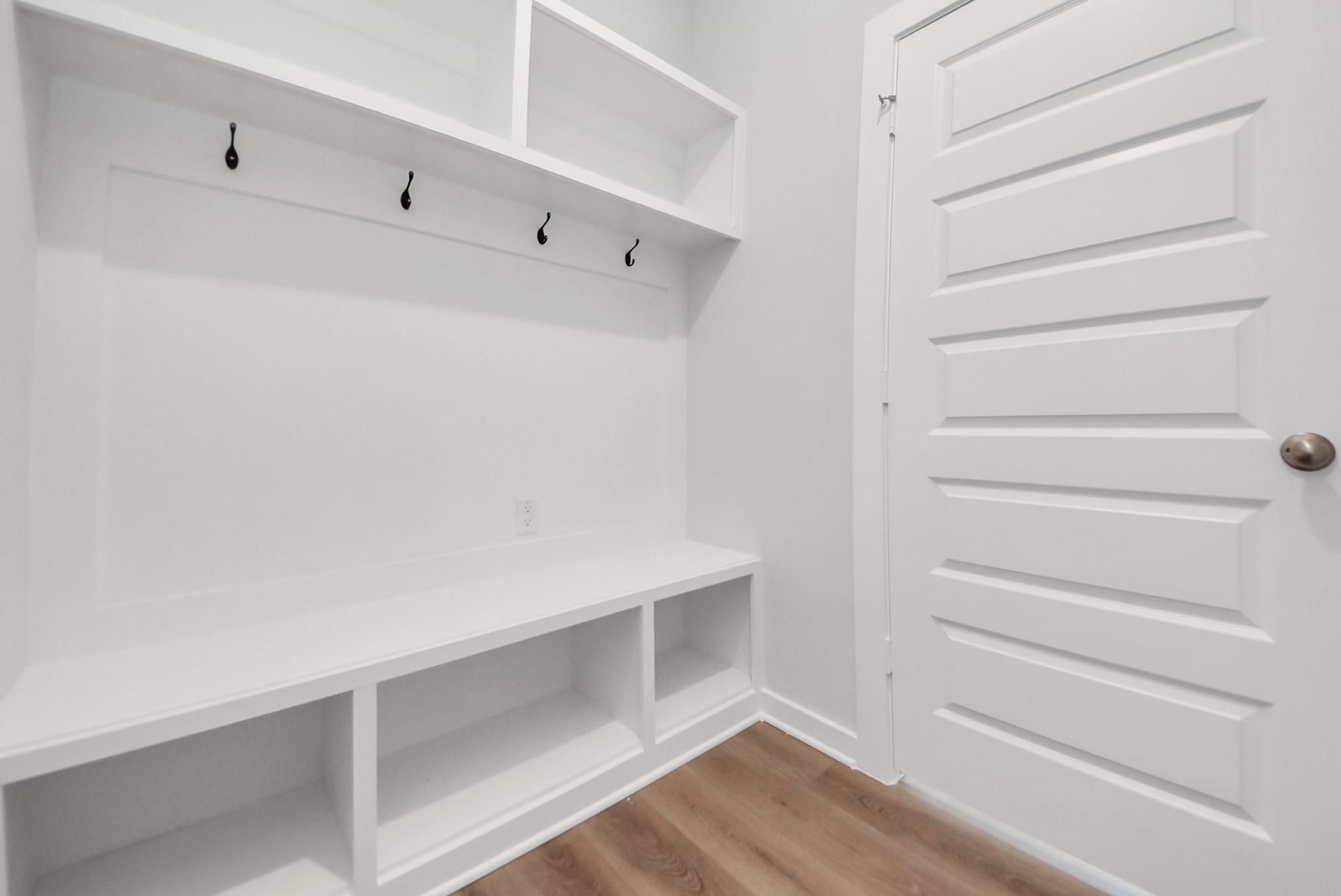Built-in white mudroom bench with cubby storage, coat hooks, and shelving in Davidson Homes The San Marcos E, Beasley, Texas