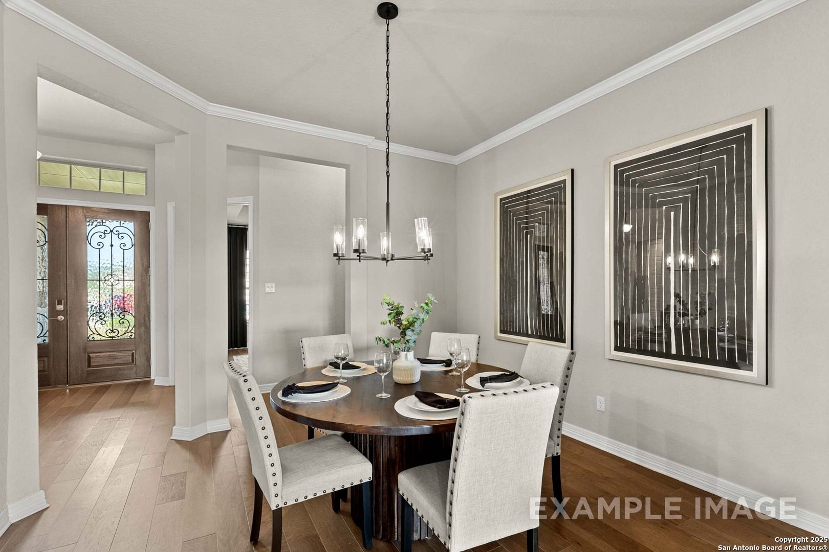 Elegant dining room with round wooden table, upholstered chairs, chandelier, abstract art, open to entryway in The Summerlin B by Davidson Homes, Castroville, Texas