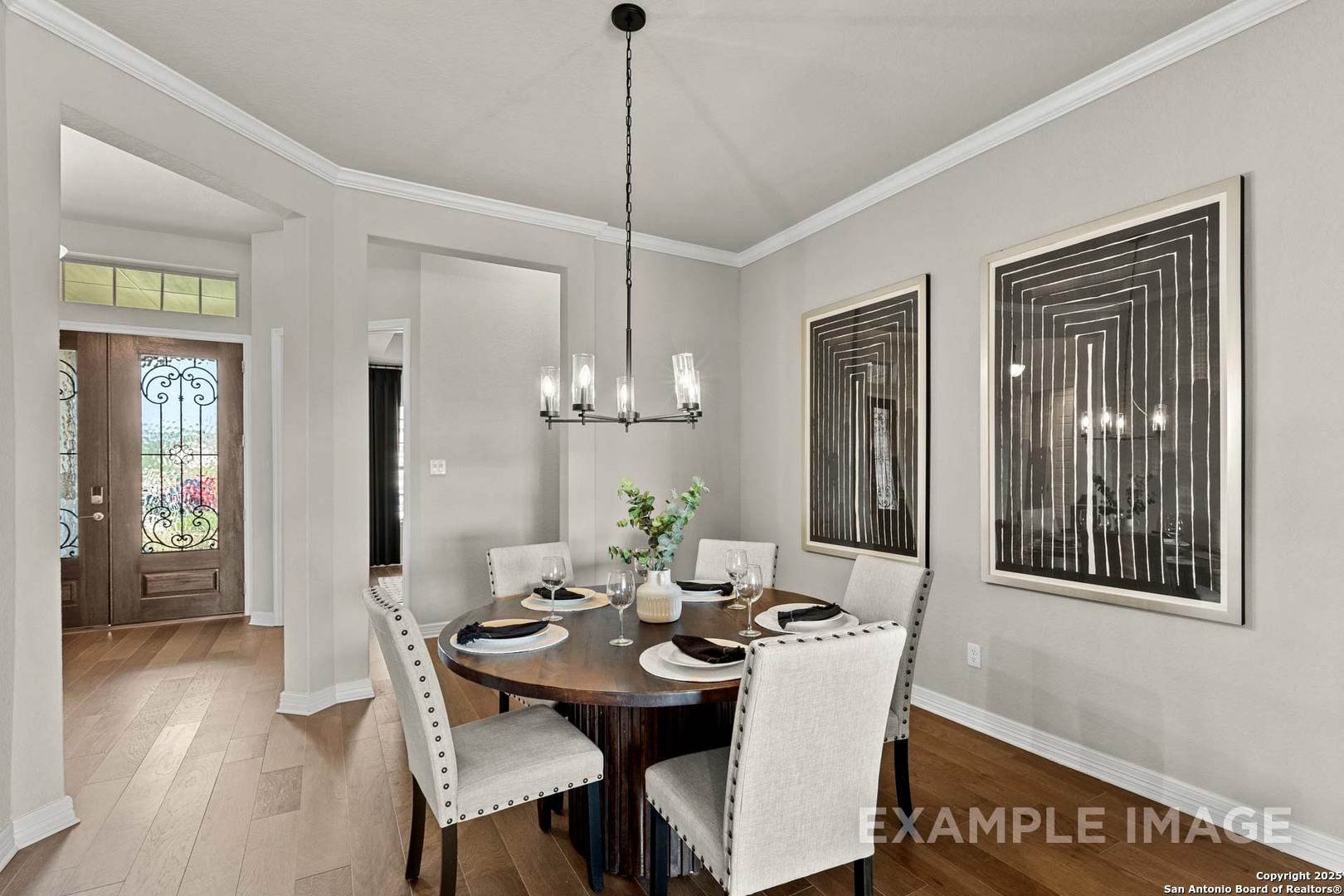 Elegant dining room with round wooden table, upholstered chairs, chandelier, abstract art, open to entryway in The Summerlin B by Davidson Homes, Castroville, Texas
