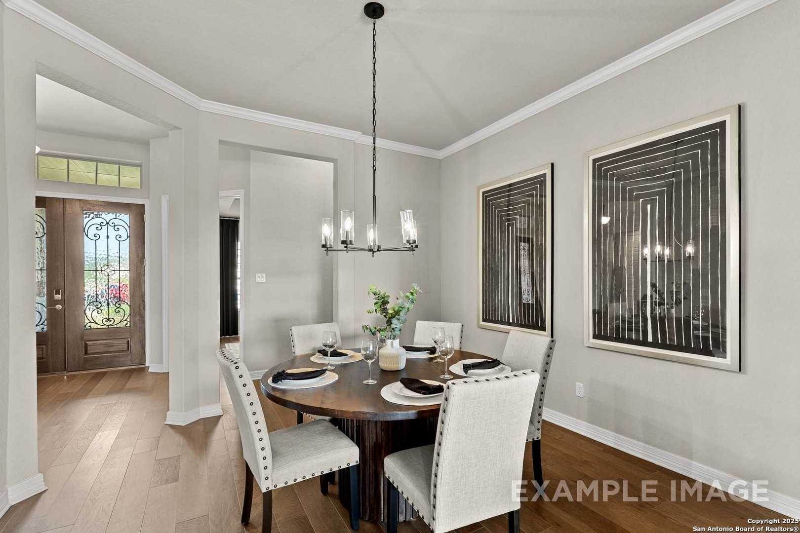 Elegant dining room with round wooden table, upholstered chairs, chandelier, abstract art, open to entryway in The Summerlin B by Davidson Homes, Castroville, Texas