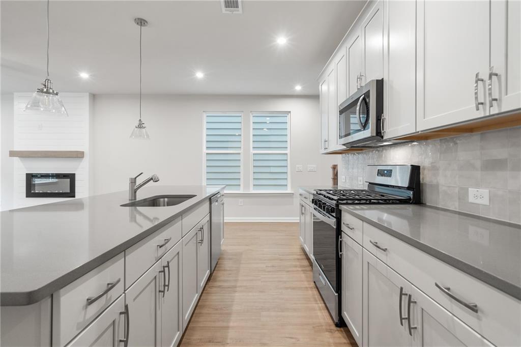 Modern kitchen with white shaker cabinets, gray quartz counters, stainless appliances, and island sink in Davidson Homes The Cary A, Kennesaw, GA