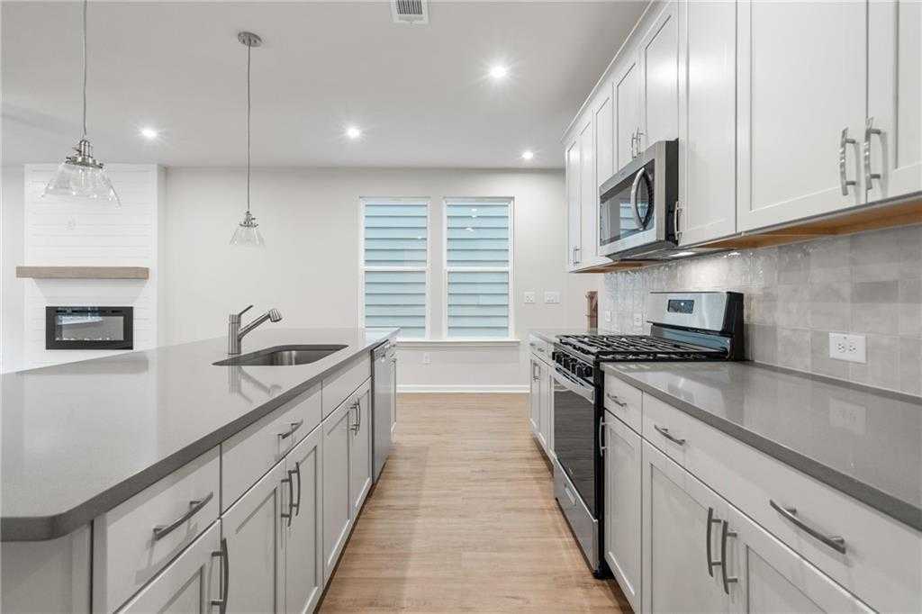 Contemporary white kitchen with quartz island, stainless appliances, and pendant lights in Davidson Homes The Cary A, Kennesaw, GA
