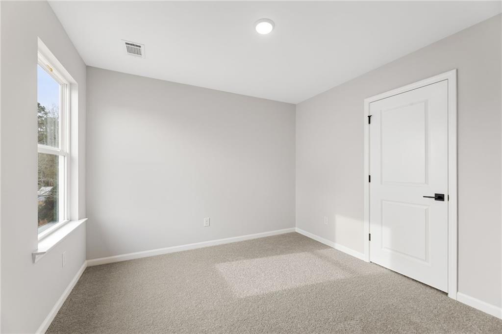 Bright empty bedroom with light gray walls, large window, white door, and carpeted floor in Davidson Homes The Rabun C, Winder, Georgia