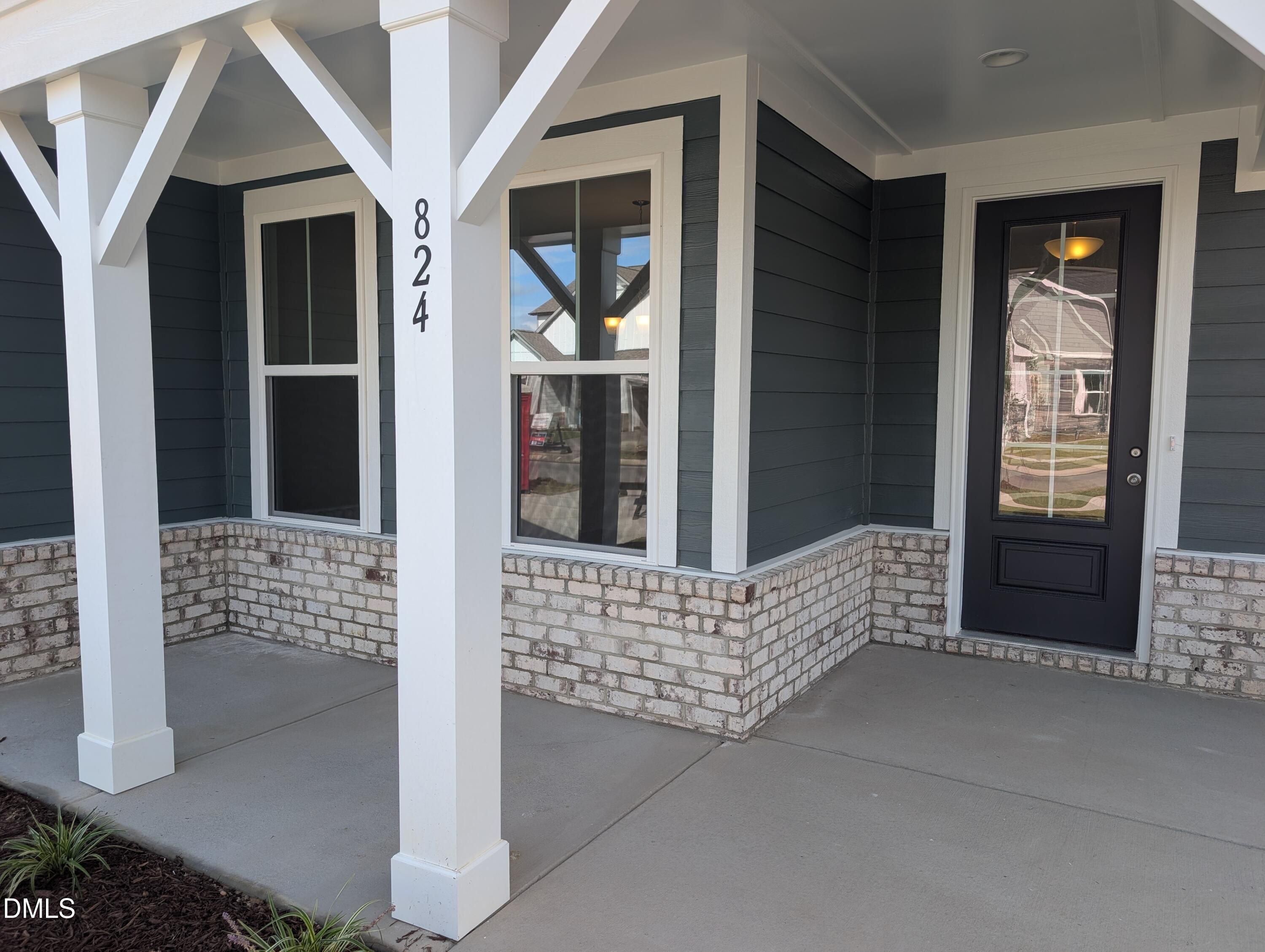 Covered front porch with white columns, brick wainscot, and black front door at Davidson Homes Magnolia A in Wendell Ridge, NC