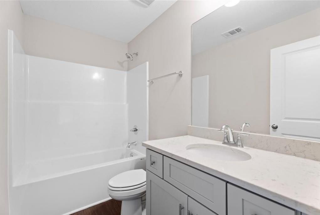 Bright bathroom with white tub-shower combo, gray vanity, sink, and toilet in Davidson Homes The Washington, Phenix City, Alabama