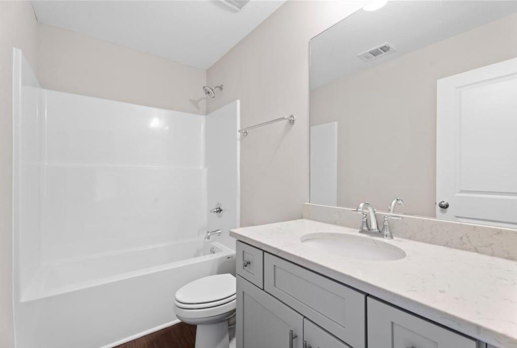 Bright bathroom with white tub-shower combo, gray vanity, sink, and toilet in Davidson Homes The Washington, Phenix City, Alabama