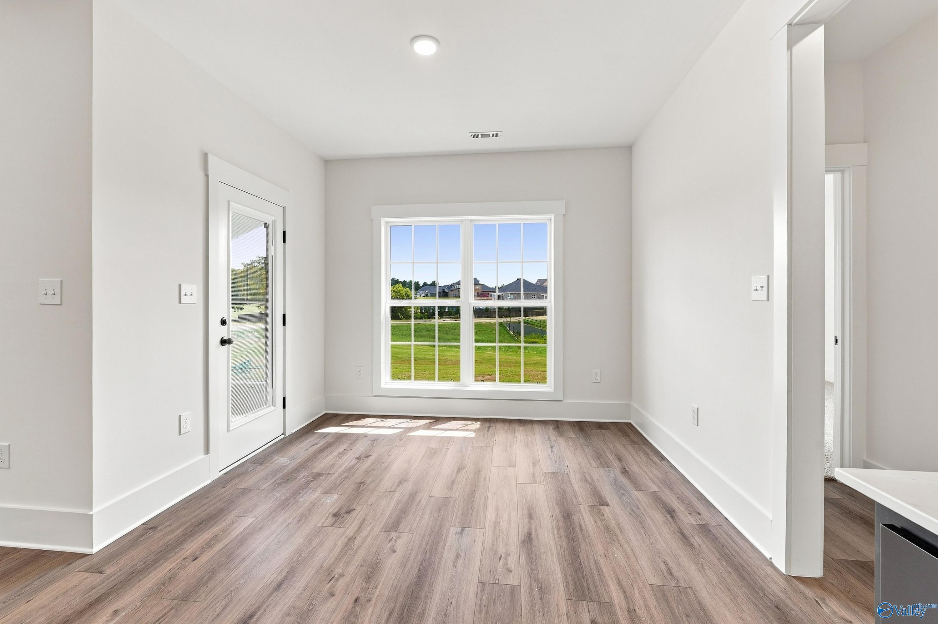 Bright dining room with luxury vinyl plank flooring, glass door, and large window overlooking backyard in Davidson Homes Valencia, Huntsville