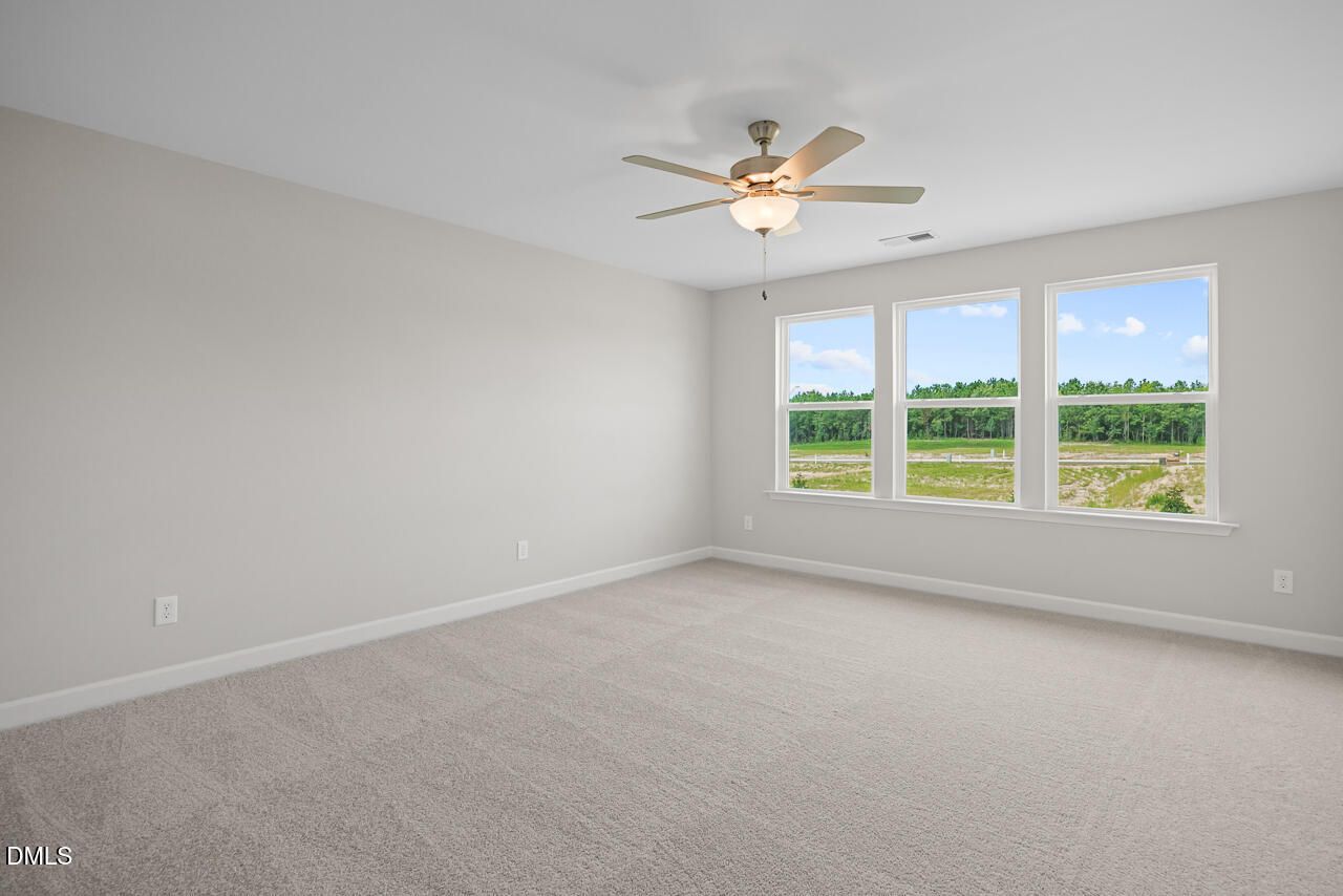 Spacious bedroom with carpet, ceiling fan, and large windows in The Chestnut floor plan at Wendell Ridge, North Carolina.