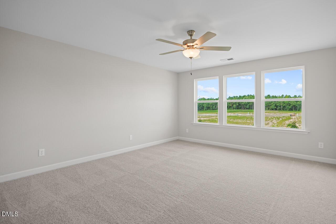 Spacious bedroom with carpet, ceiling fan, and large windows in The Chestnut floor plan at Wendell Ridge, North Carolina.