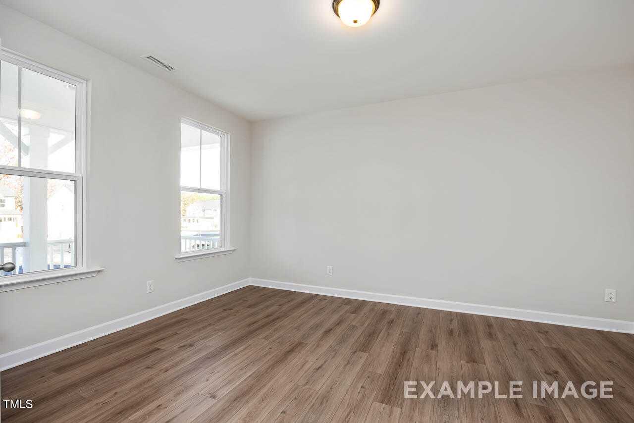 Bright empty bedroom with hardwood floors, white walls, and large windows to porch in Davidson Homes Hickory II B, Lillington, NC