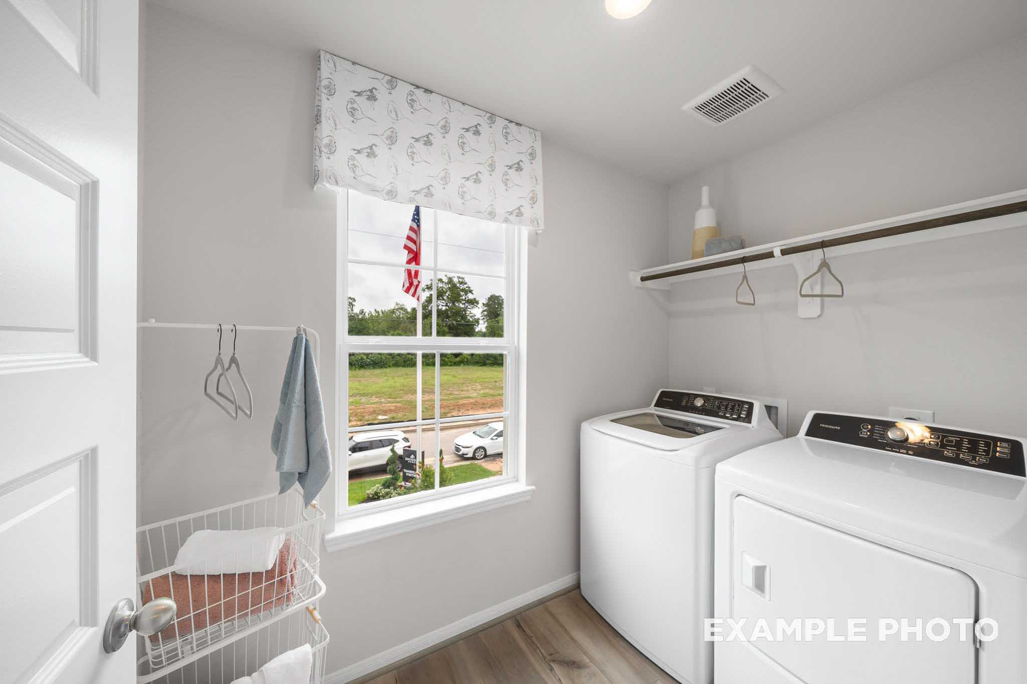 Spacious laundry room in The Trinity floor plan with white washer-dryer set, storage shelves, and window view