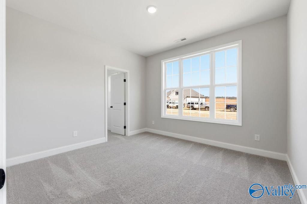 Bright empty bedroom with light gray walls, gray carpet, and large triple-window overlooking field in Davidson Homes The Montgomery B, Hartselle, Alabama