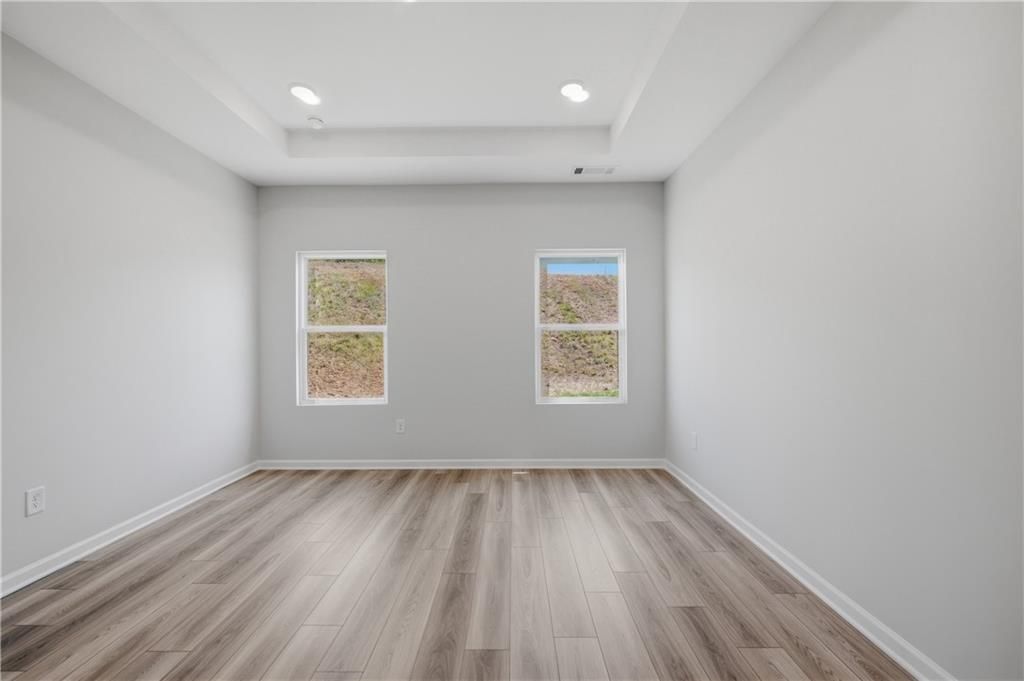 Bright empty bedroom with wood-look flooring, tray ceiling, and dual windows in Davidson Homes The Oconee B, Canton, Georgia
