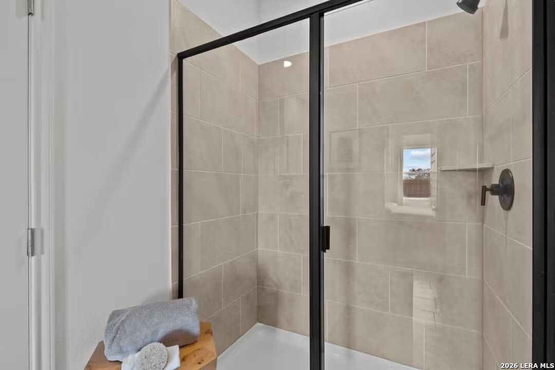 Modern frameless glass shower with beige tiles, bench, and window in master bathroom, Davidson Homes Douglas C, Converse TX