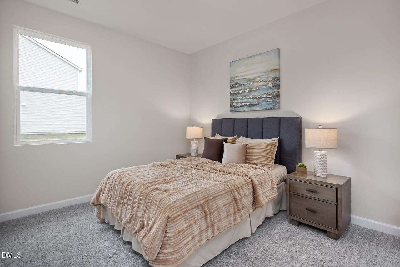 Cozy bedroom with queen bed, beige bedding, navy upholstered headboard, lamps on wooden nightstands, abstract wall art in Davidson Homes The Carter C, Lillington NC