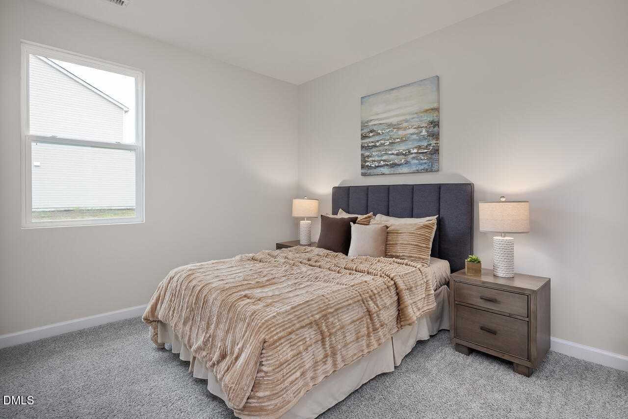 Cozy bedroom with beige bedding on dark blue upholstered headboard, lamps on wood nightstands, and abstract art in The Carter C by Davidson Homes, Lillington, NC