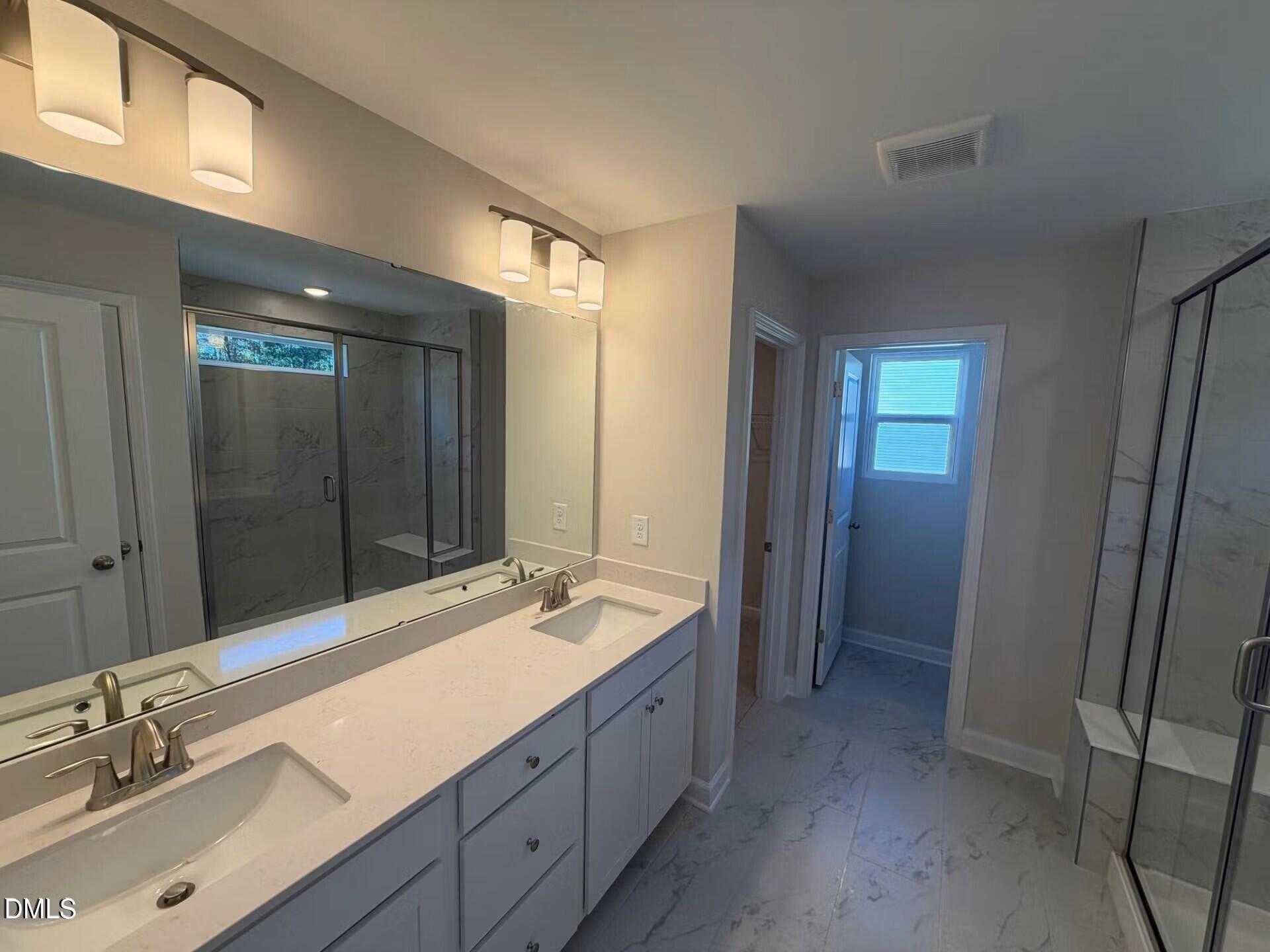 Modern master bathroom featuring double vanity, large mirror, and frameless glass shower in The Gavin C, Lillington, NC