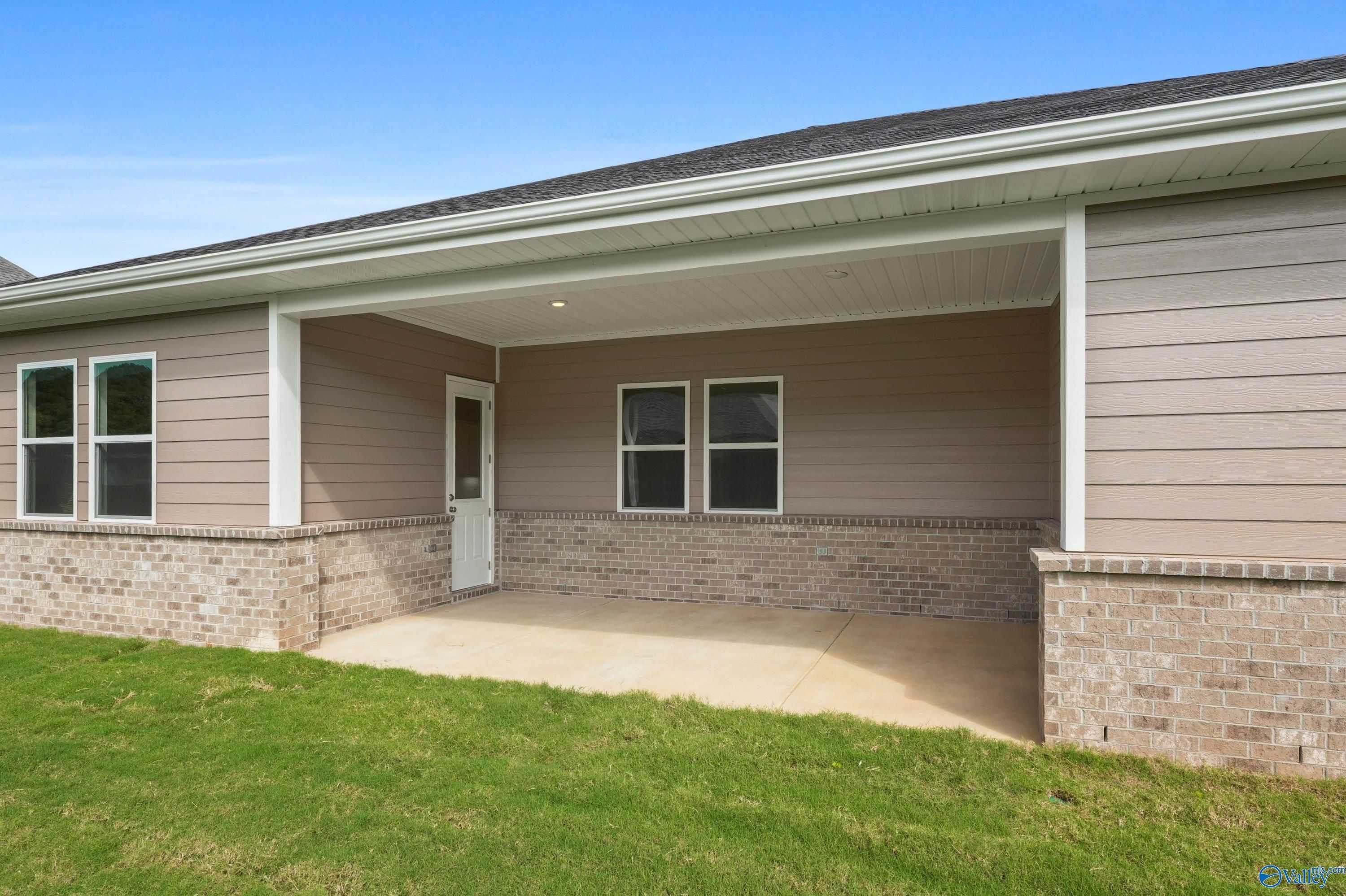 Covered side porch with beige siding, brick accents, glass door, and windows on Evermore Homes The Haven in Owens Cross Roads, Alabama
