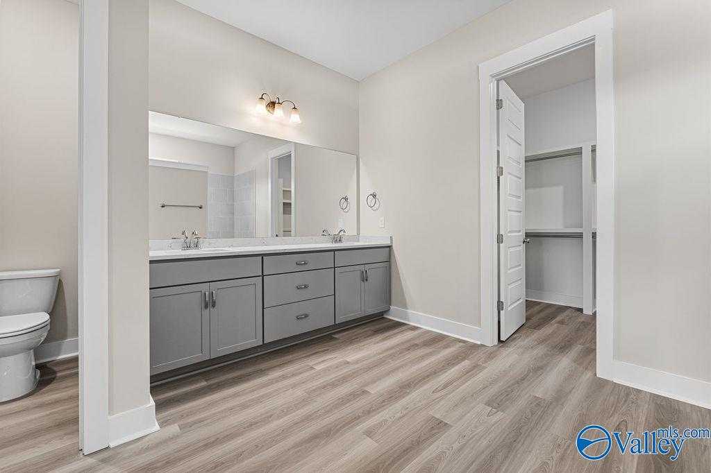 Modern bathroom with double gray vanity, large mirror, sconce lighting, toilet, and open closet in Evermore Homes The Oxford, Owens Cross Roads, AL